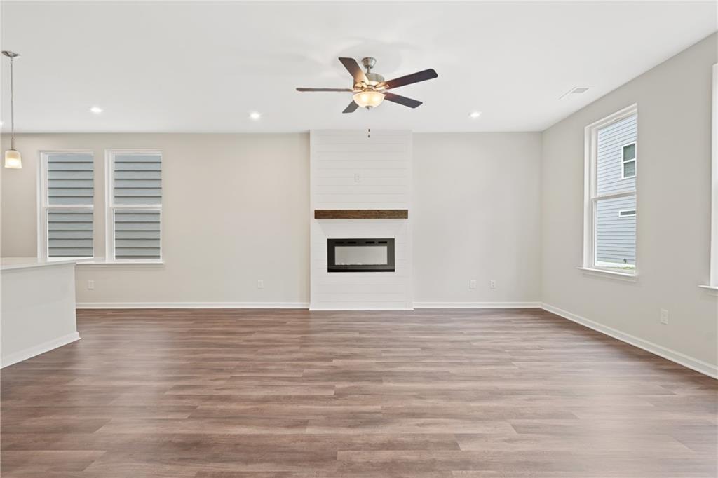 Spacious great room with white brick fireplace, ceiling fan, hardwood floors, and large windows in Davidson Homes The Cary B, Kennesaw, Georgia
