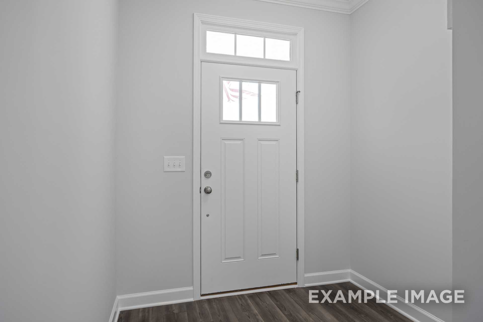 Spacious entryway of The Grace C home featuring white paneled front door with transom window and hardwood floors