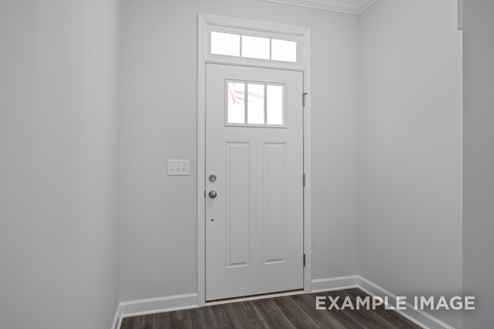 Spacious entryway of The Grace C home featuring white paneled front door with transom window and hardwood floors