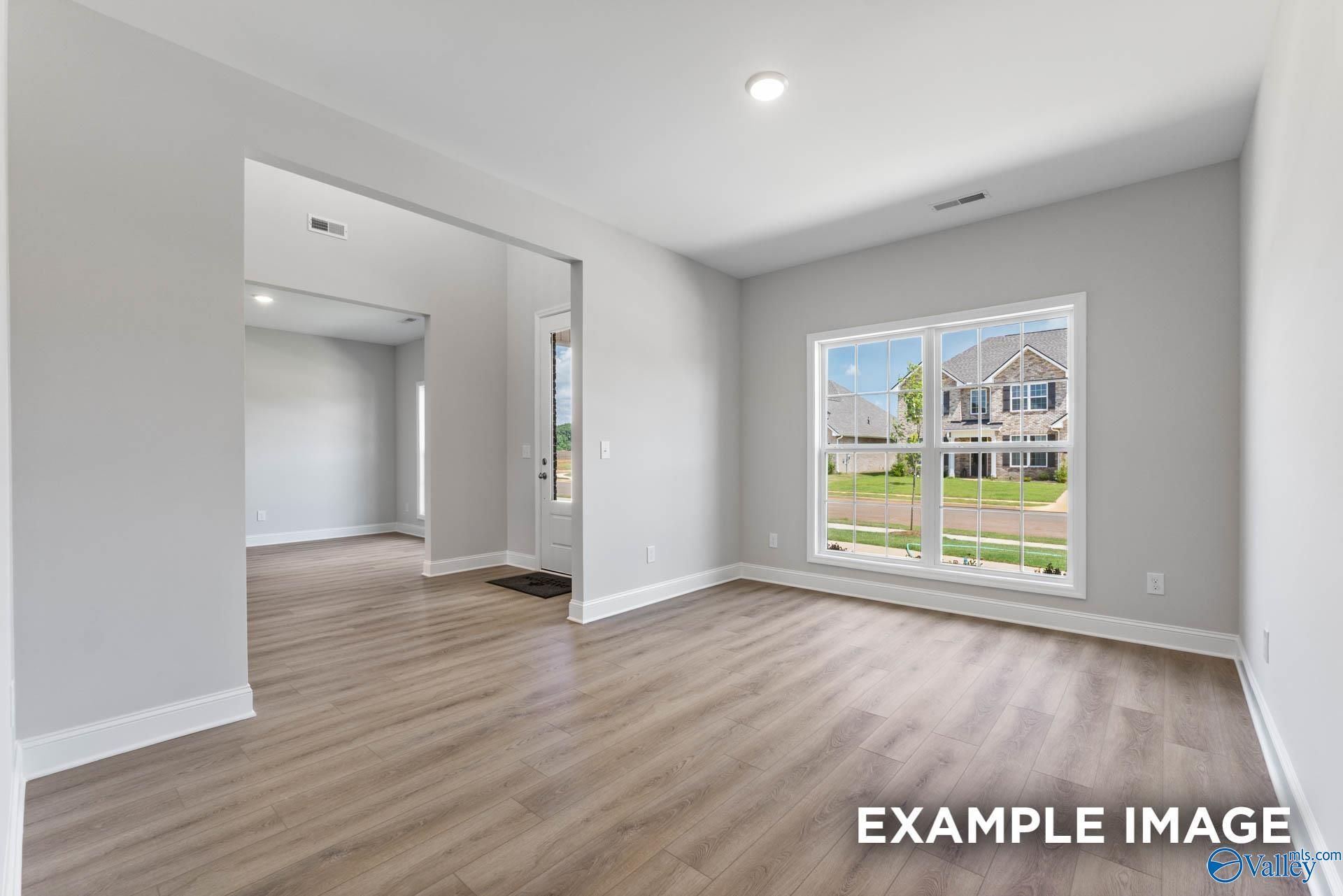 Bright living room with hardwood floors, gray walls, and large window to backyard in 5-bedroom Davidson Homes The Madison A, Meridianville, AL