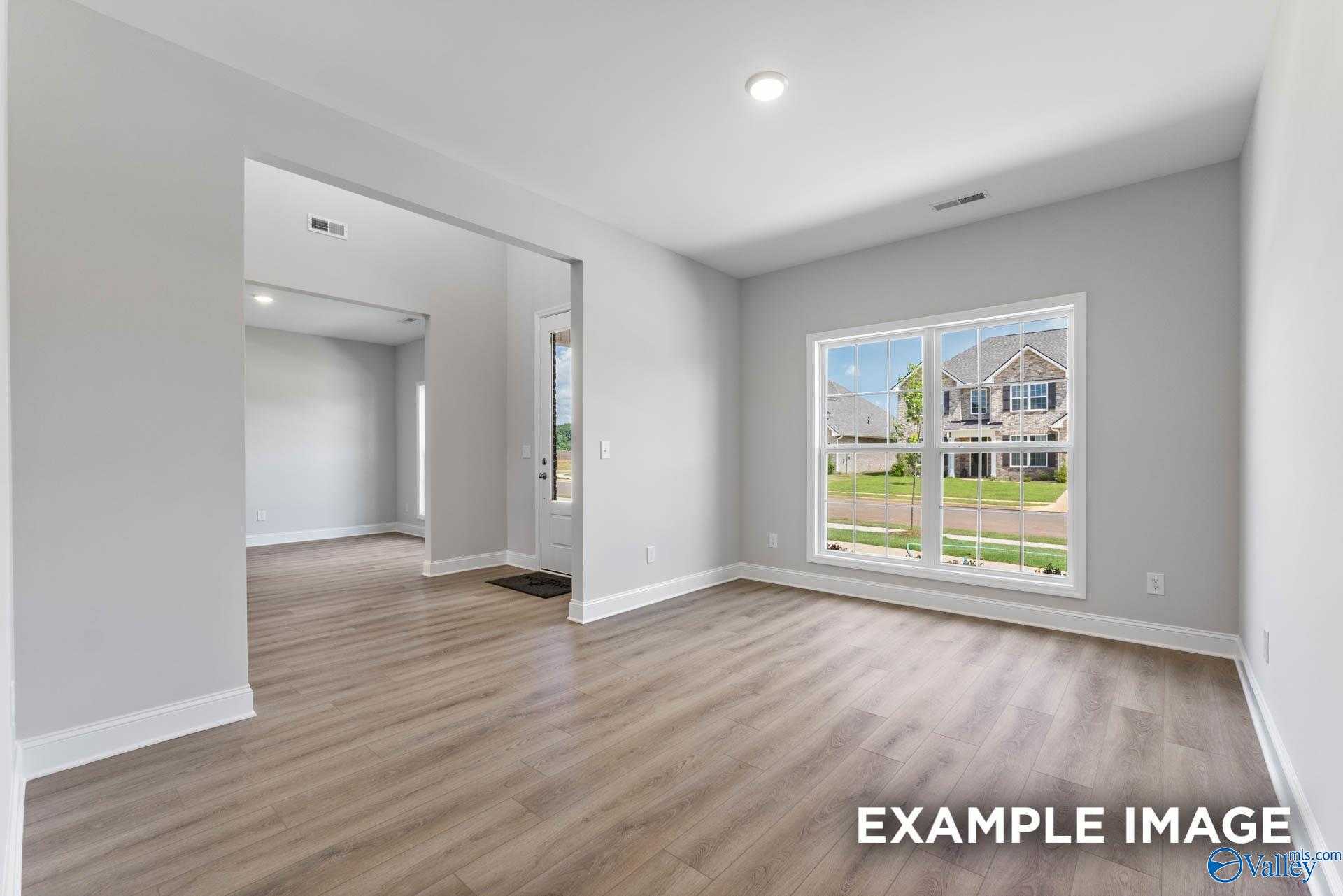 Spacious empty living room with gray walls, hardwood floors, and large window overlooking neighborhood in Davidson Homes Madison A, Harvest, Alabama