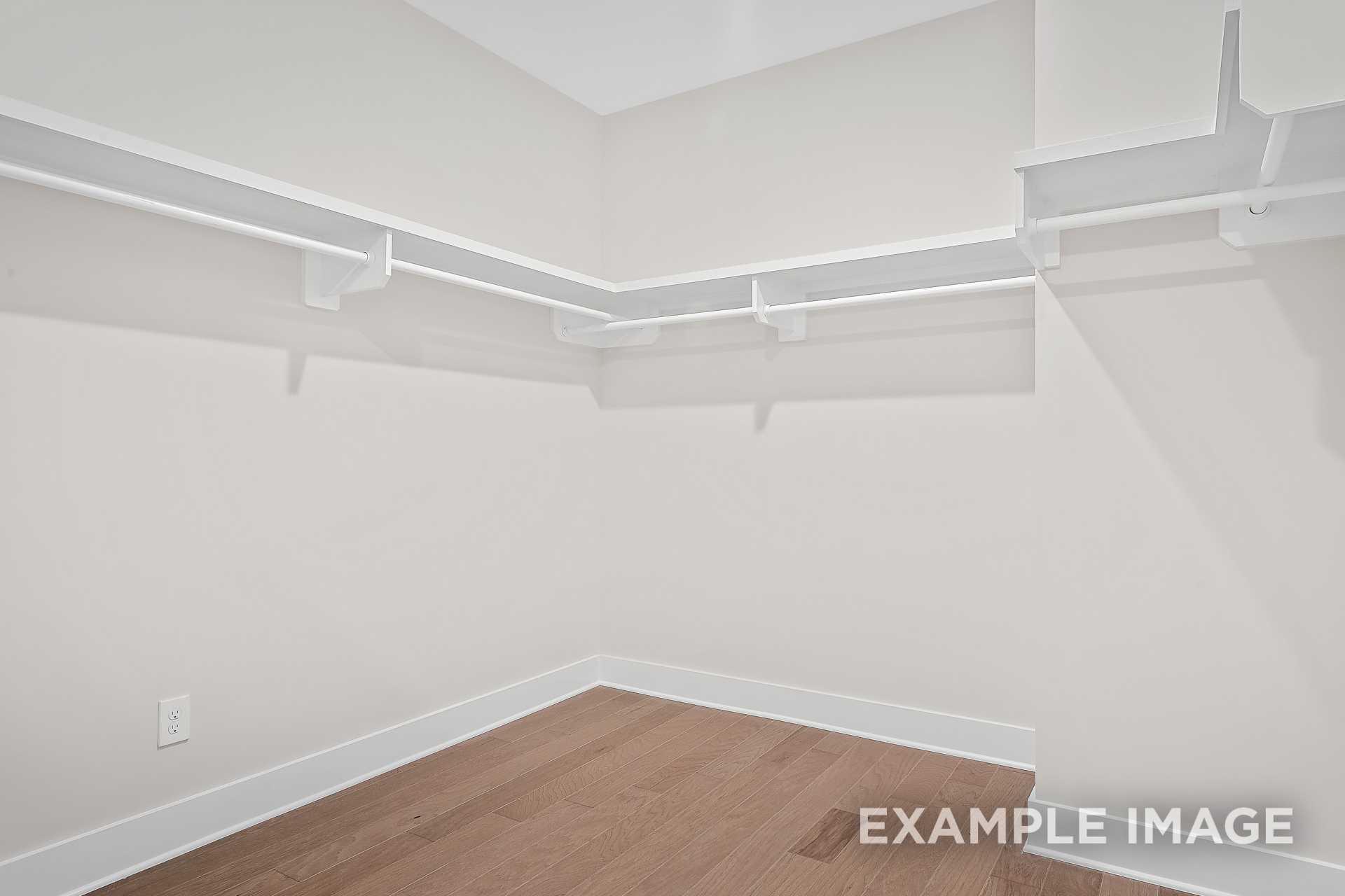 Spacious walk-in closet in The Hawkins master suite featuring white shelving, beige walls, and hardwood floors