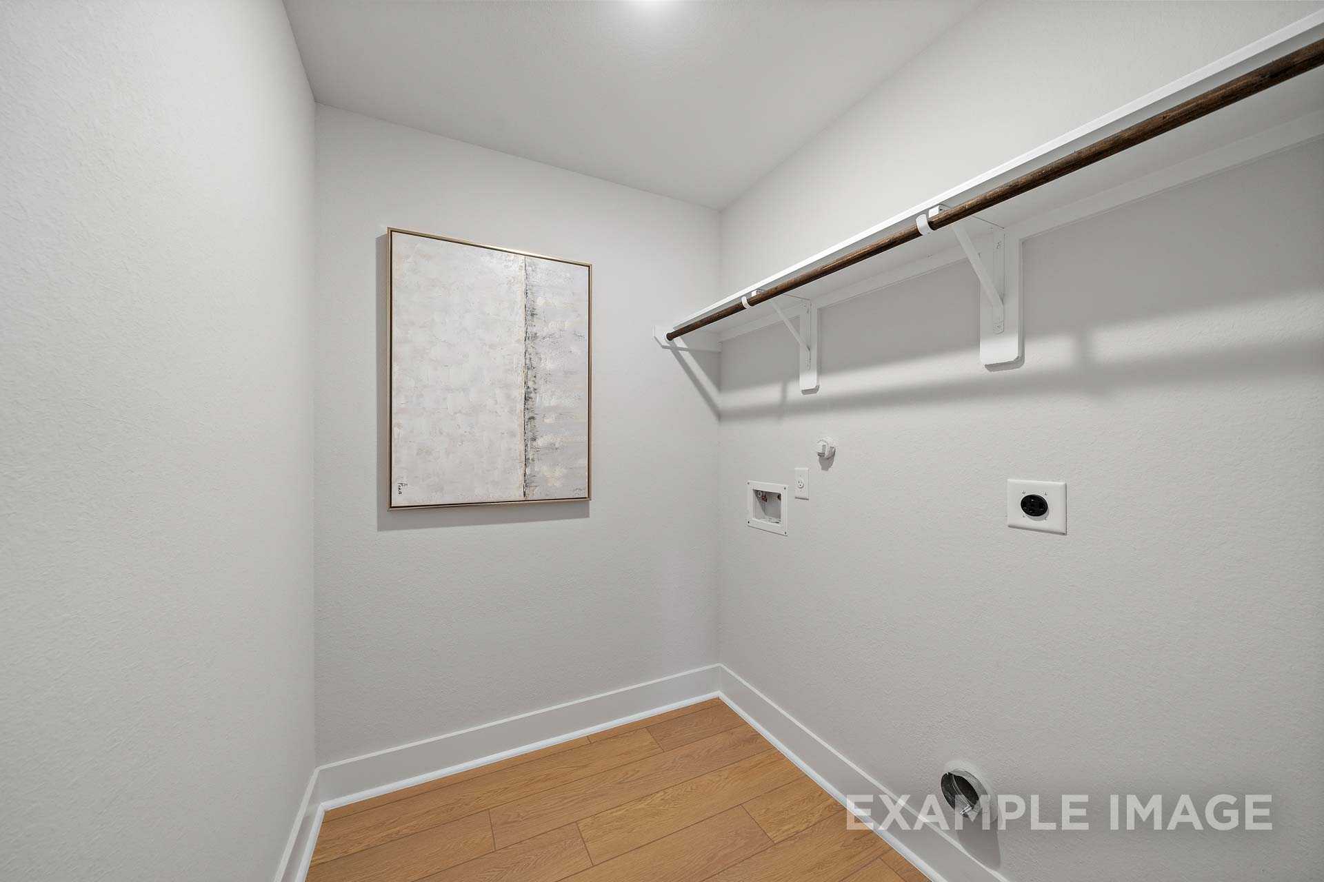 Spacious laundry room in The Rose B home by Davidson Homes with white shelving, hanging rod, washer-dryer hookups, abstract wall art, and hardwood floors