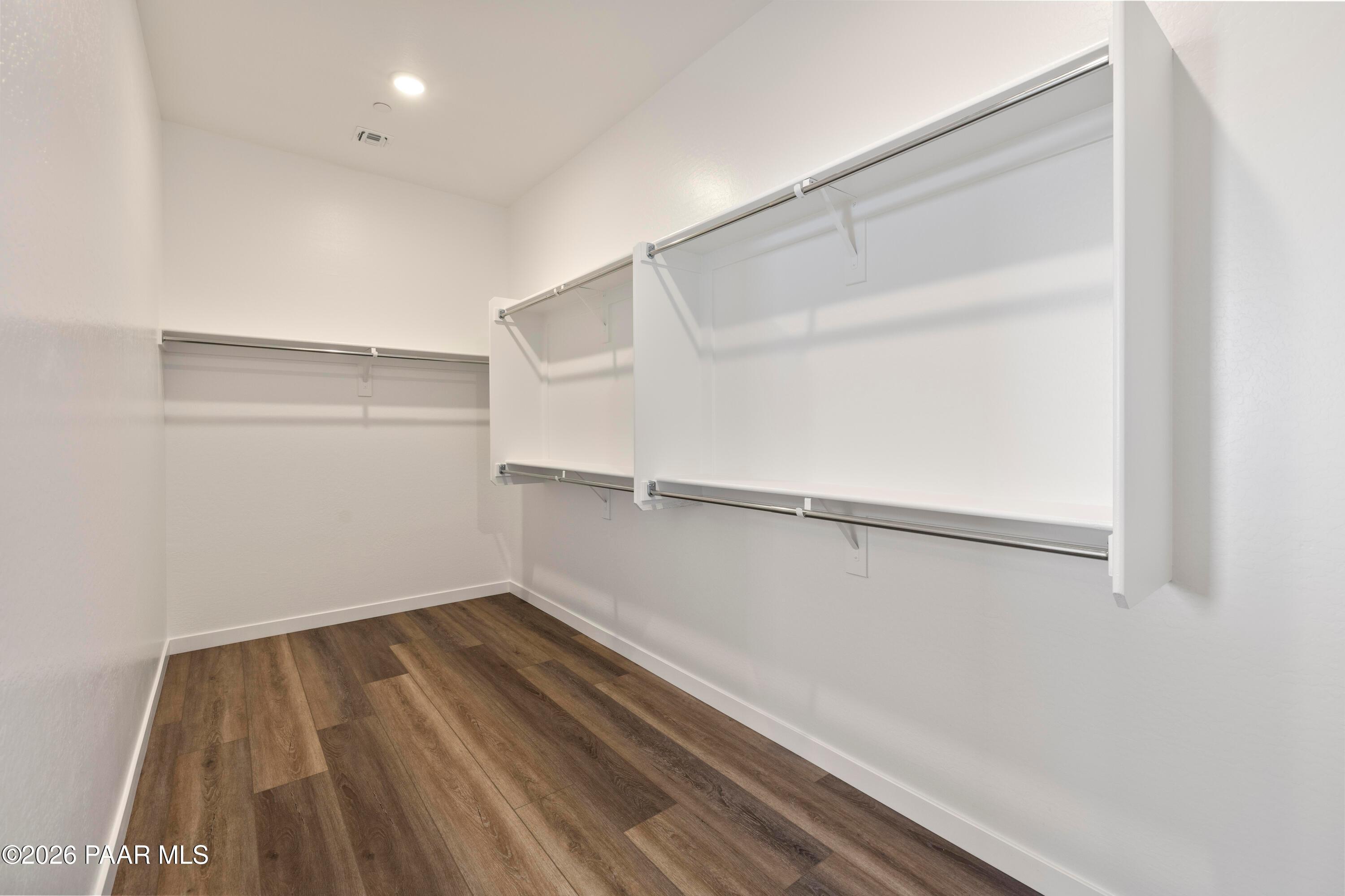 Spacious walk-in closet with white shelving, hanging rods, and hardwood floors in Davidson Homes Soleil E, Prescott AZ