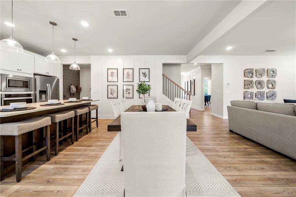 Open-concept kitchen dining living area with white cabinets island bar stools wooden table gray sofa in Davidson Homes The Hickory B Riverwood Dallas Georgia