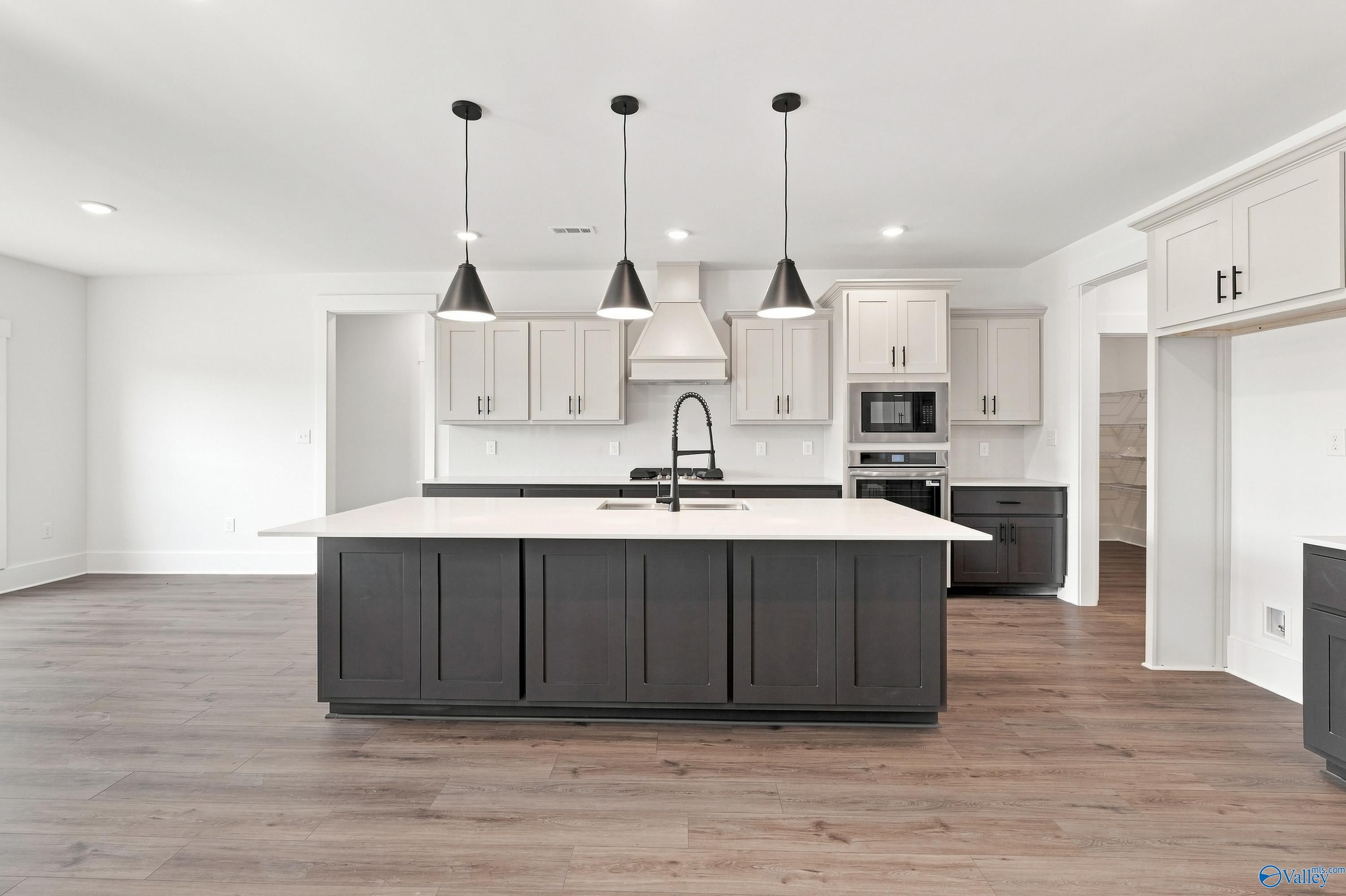 Modern kitchen with large dark island, white cabinetry, pendant lights, and luxury vinyl plank flooring in Davidson Homes' The Valencia floor plan, Huntsville, Alabama
