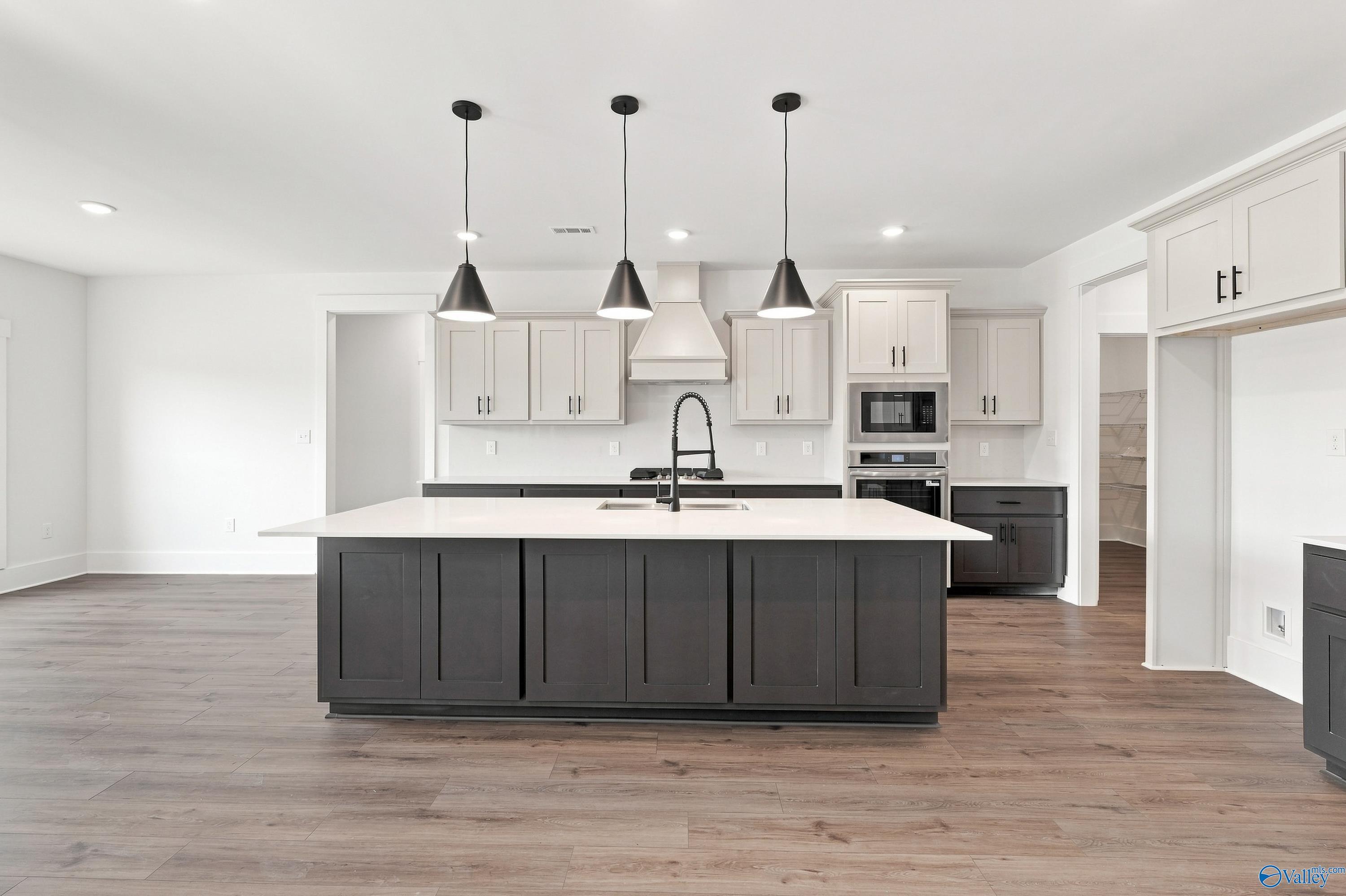 Modern kitchen with large dark island, white cabinetry, pendant lights, and luxury vinyl plank flooring in Davidson Homes' The Valencia floor plan, Huntsville, Alabama