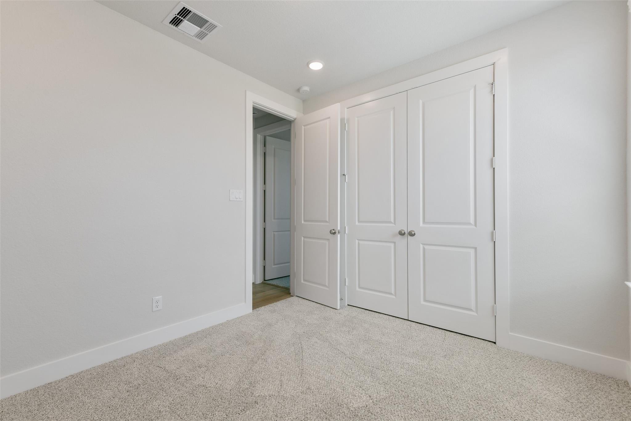 Bright secondary bedroom with white double closet doors, beige carpet, and adjoining bath in Davidson Homes The Edward A, Lago Mar, Texas City