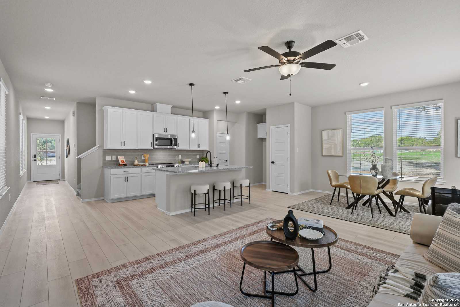 Open-concept kitchen with white cabinets, stainless microwave, island bar stools, adjacent dining and living room in The Charlotte B, San Antonio, TX