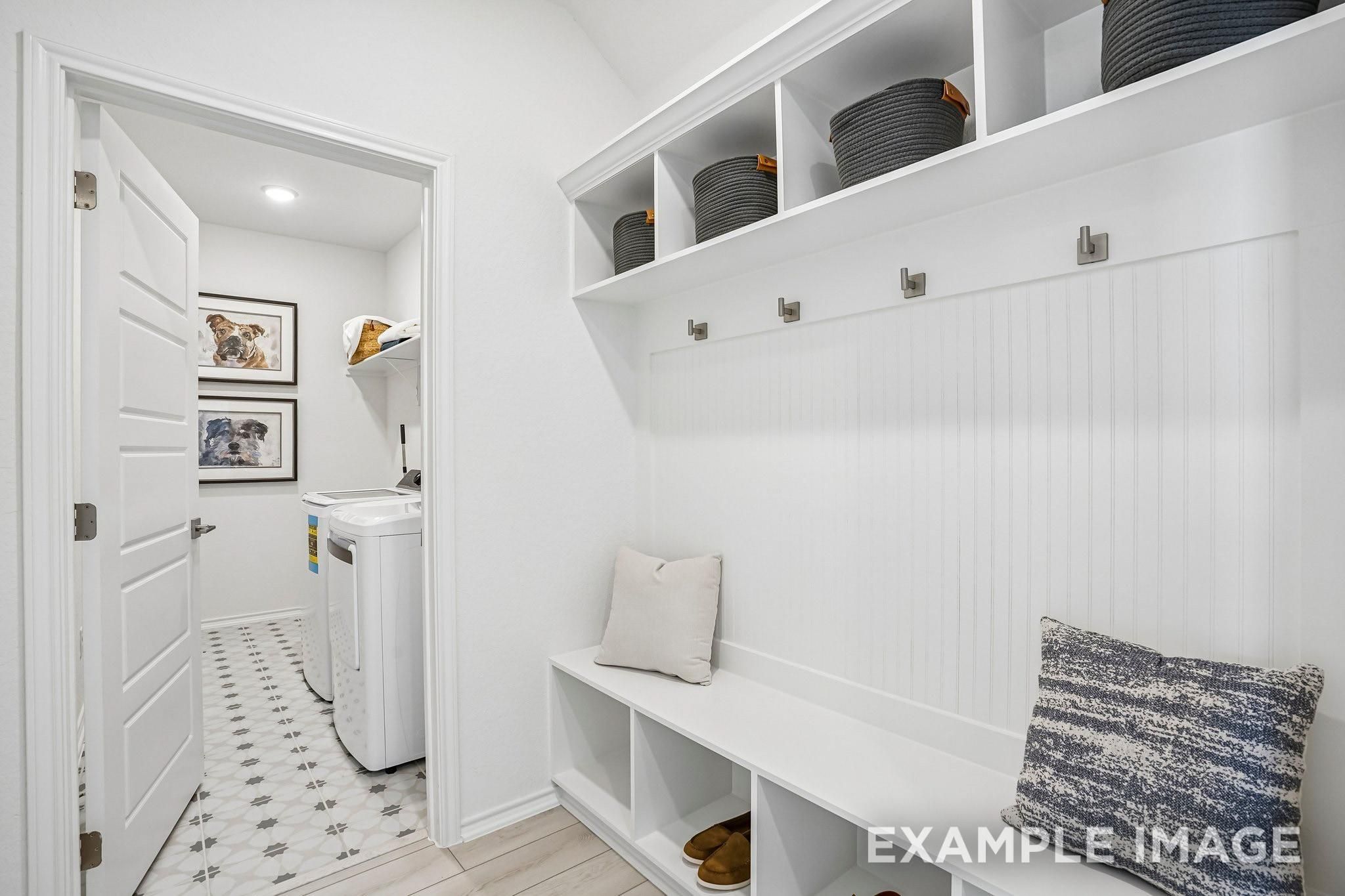 White mudroom bench with cubbies and coat hooks beside laundry room in Davidson Homes Ashport J, Sundance Cove, Crosby TX