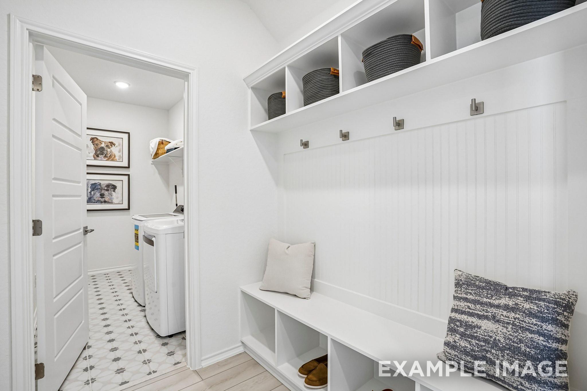 White mudroom bench with cubbies and coat hooks beside laundry room in Davidson Homes Ashport J, Sundance Cove, Crosby TX