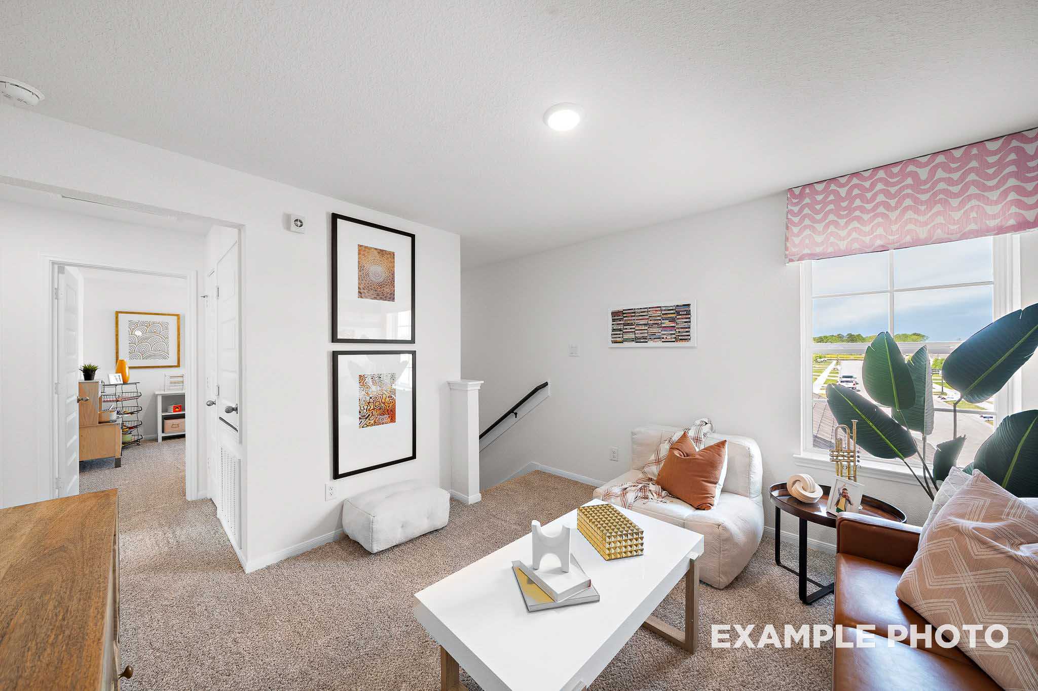 Cozy upstairs loft in The Sabine E showcasing beige armchair, white coffee table, wall art, and large window with plant view