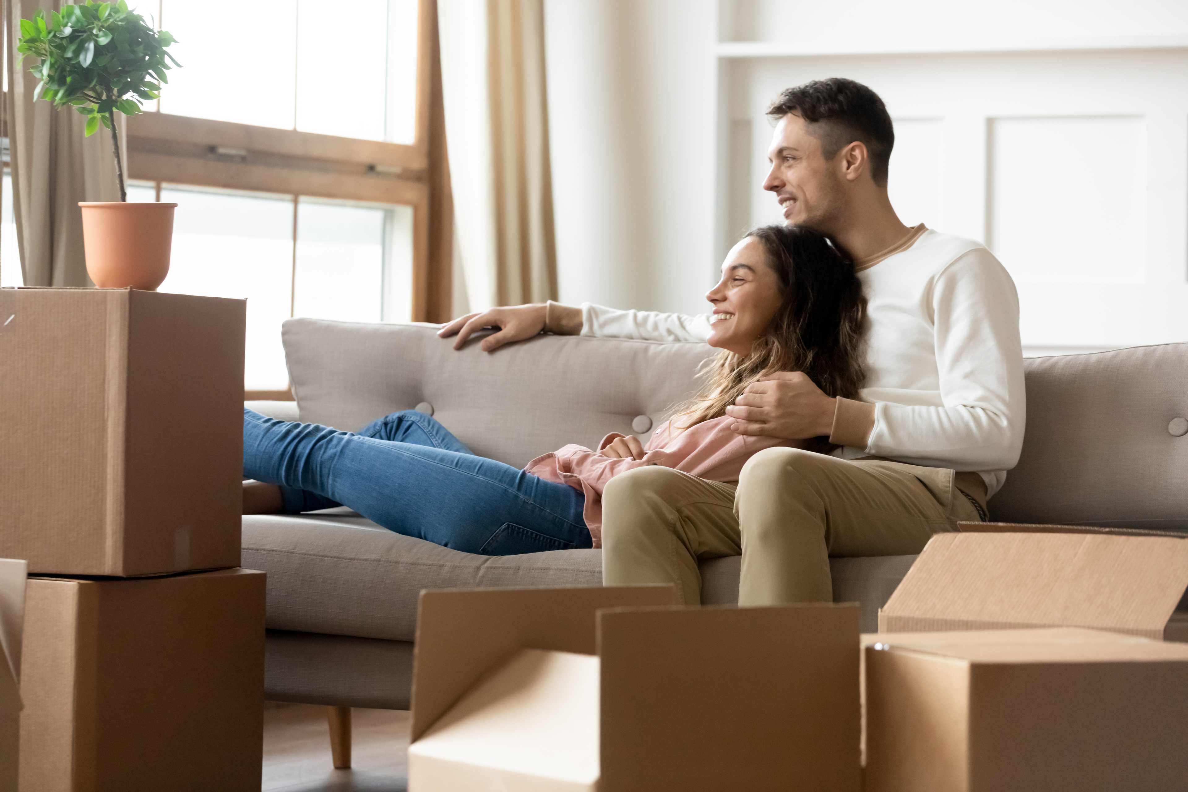 Happy couple cuddling on sofa in new Davidson Homes living room at The Village at Shallowford Kennesaw GA amid moving boxes
