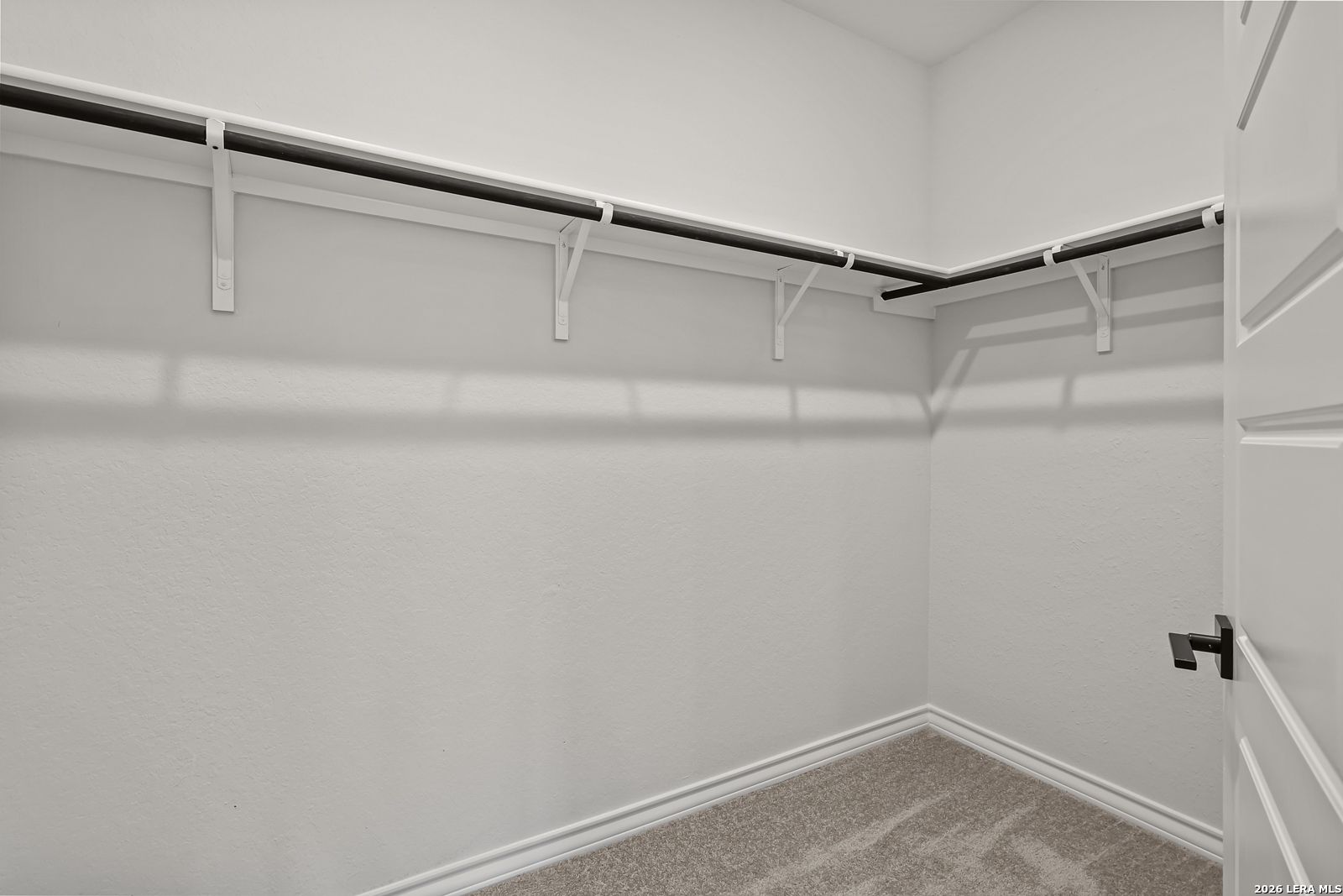Corner walk-in closet with dual hanging rods and carpeted floor in Davidson Homes The Oxford F, Castroville, Texas