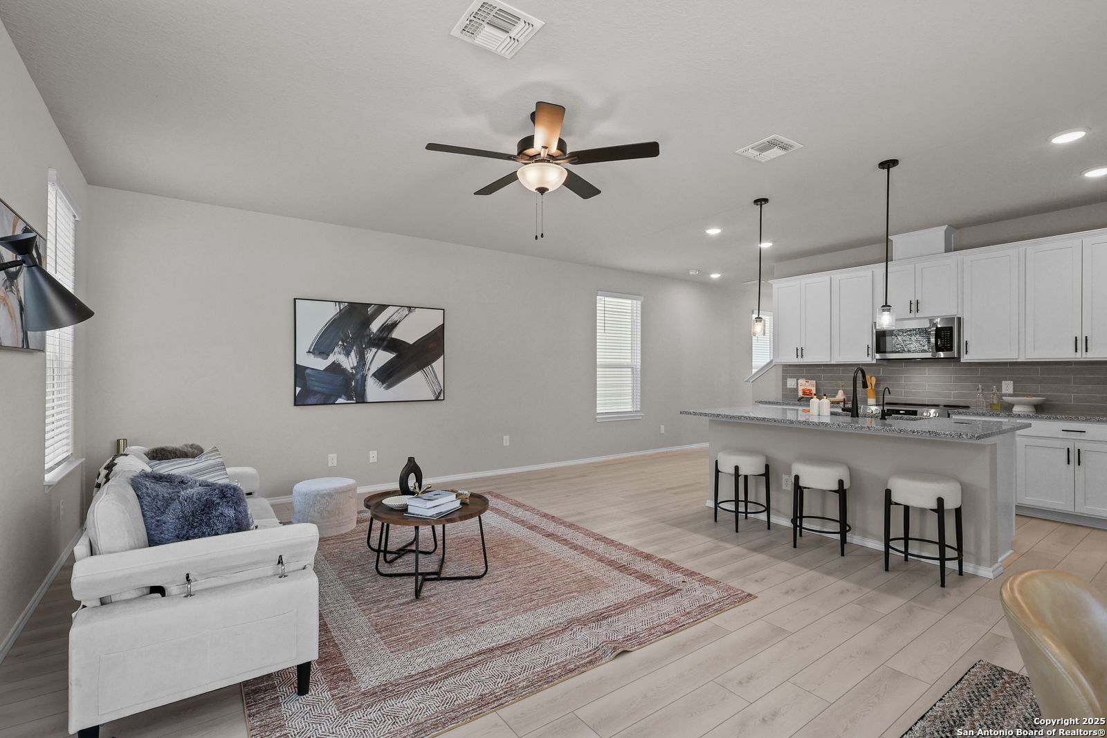 Open-concept living room with white sofa, ceiling fan, and kitchen island in Davidson Homes The Charlotte B, San Antonio