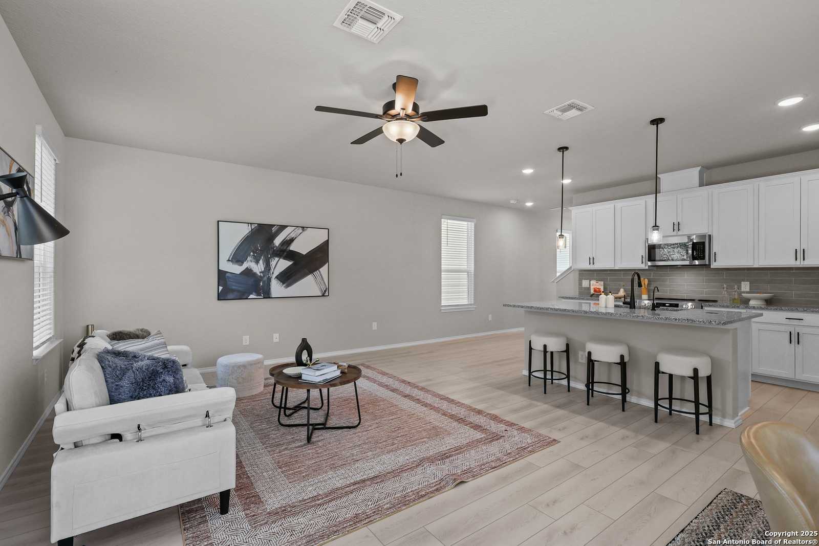 Open-concept living room with white sofa, ceiling fan, and kitchen island in Davidson Homes The Charlotte B, San Antonio
