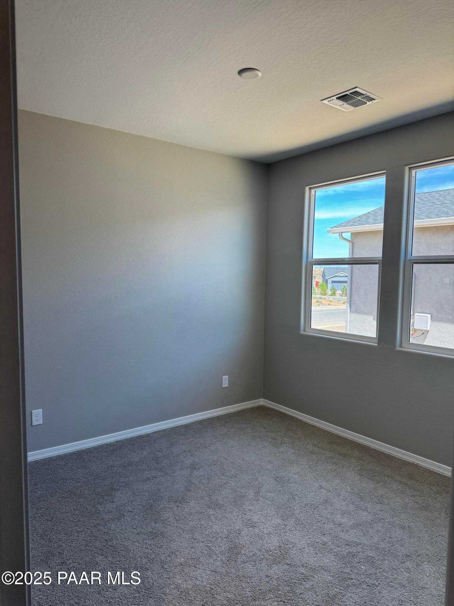 Empty secondary bedroom with gray walls, plush gray carpet, and large windows overlooking Prescott neighborhood in The Sheridan II B