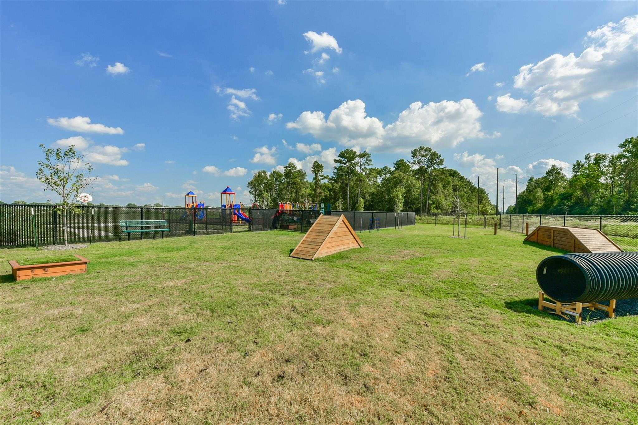 Community dog park with agility A-frame, tunnel, jumps and fenced grassy play area near colorful playground in The Villages at WestPointe, Dayton, Texas