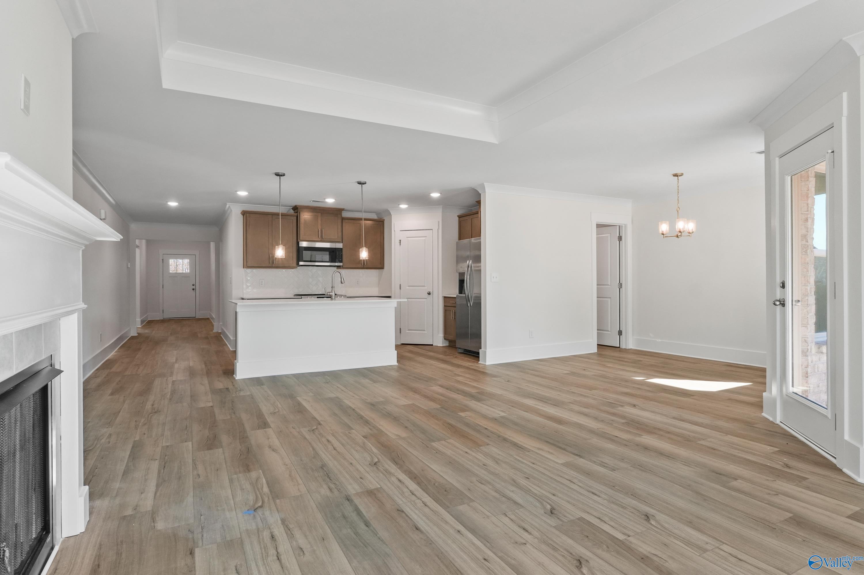 Spacious open-concept living room with white fireplace, kitchen island, stainless appliances, hardwood floors in Davidson Homes The Daphne C, Arab AL