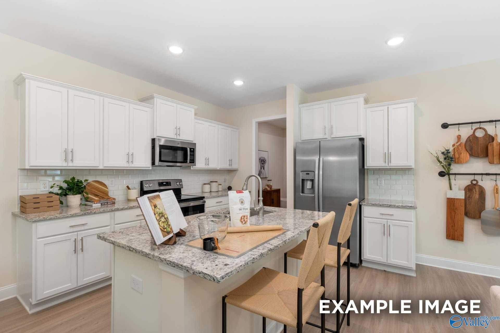Modern white kitchen with granite island, stainless appliances, and bar seating in The Camden B home, Davidson Homes Huntsville AL