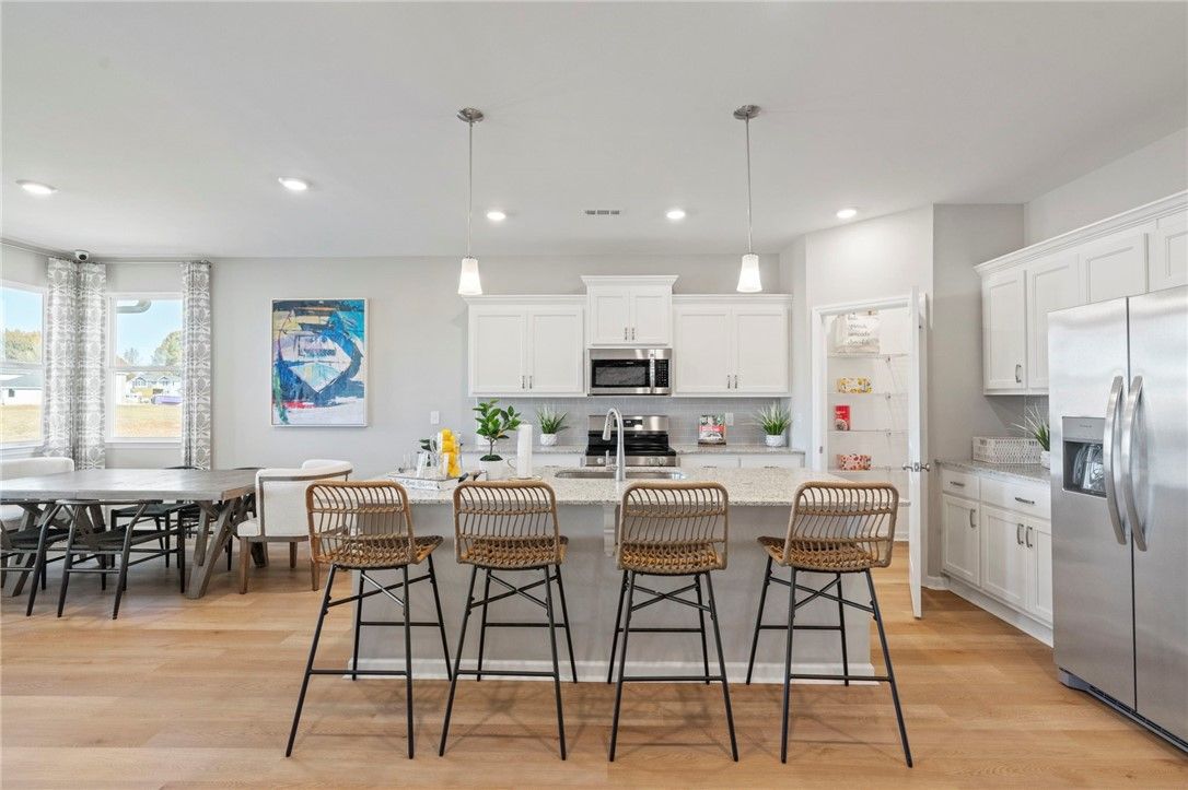 Bright open-concept kitchen with white cabinets, stainless appliances, and rattan island stools in The Phoenix B, Opelika AL