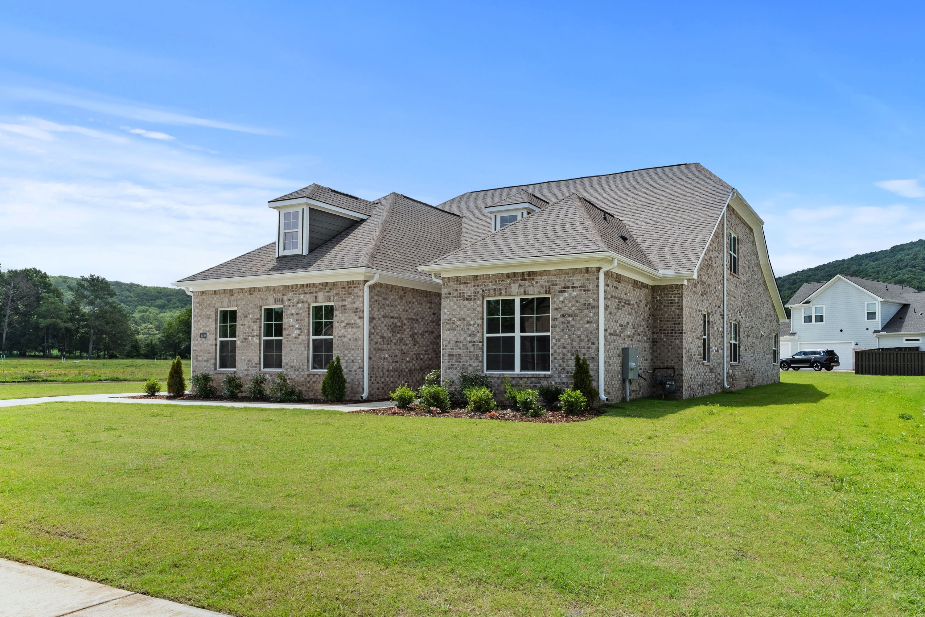 Two-story brick home The Oxford A by Evermore Homes, Owens Cross Roads Alabama, gabled roof, dormer windows, lush green lawn, shrubs