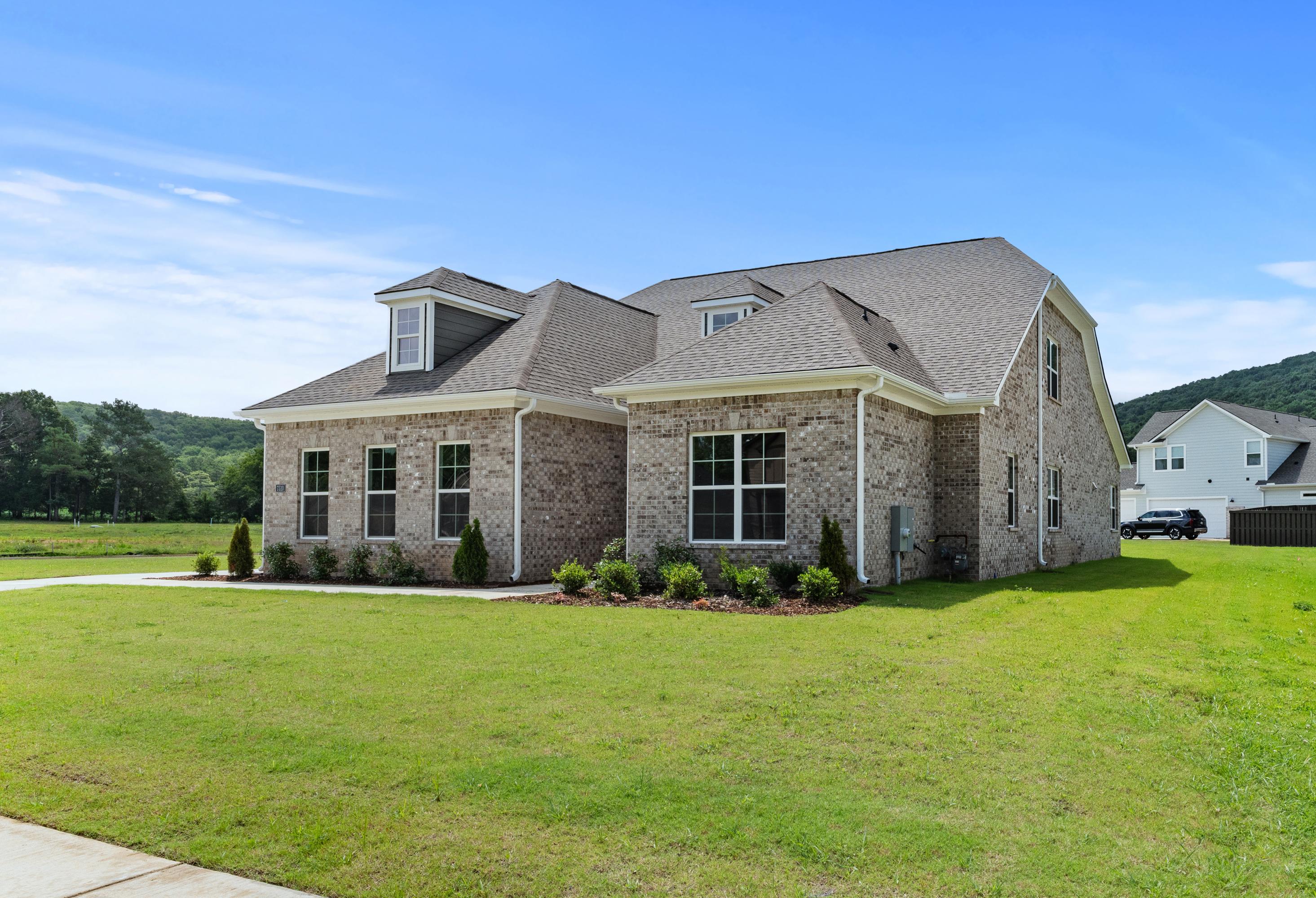 Two-story brick home The Oxford A by Evermore Homes, Owens Cross Roads Alabama, gabled roof, dormer windows, lush green lawn, shrubs