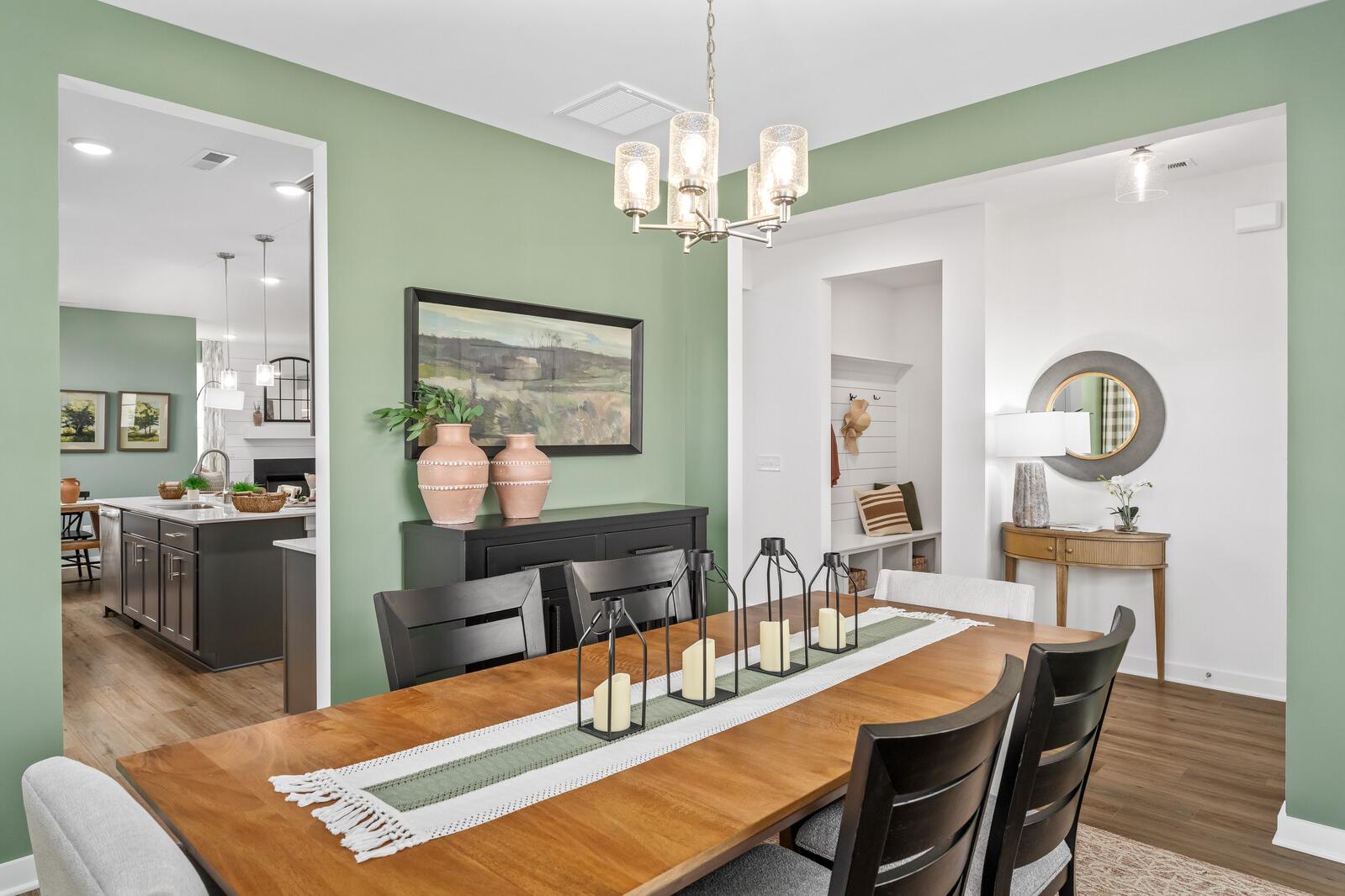 Elegant dining room at Calista Farms in White House TN featuring sage green walls, wooden table with black chairs, chandelier, and art