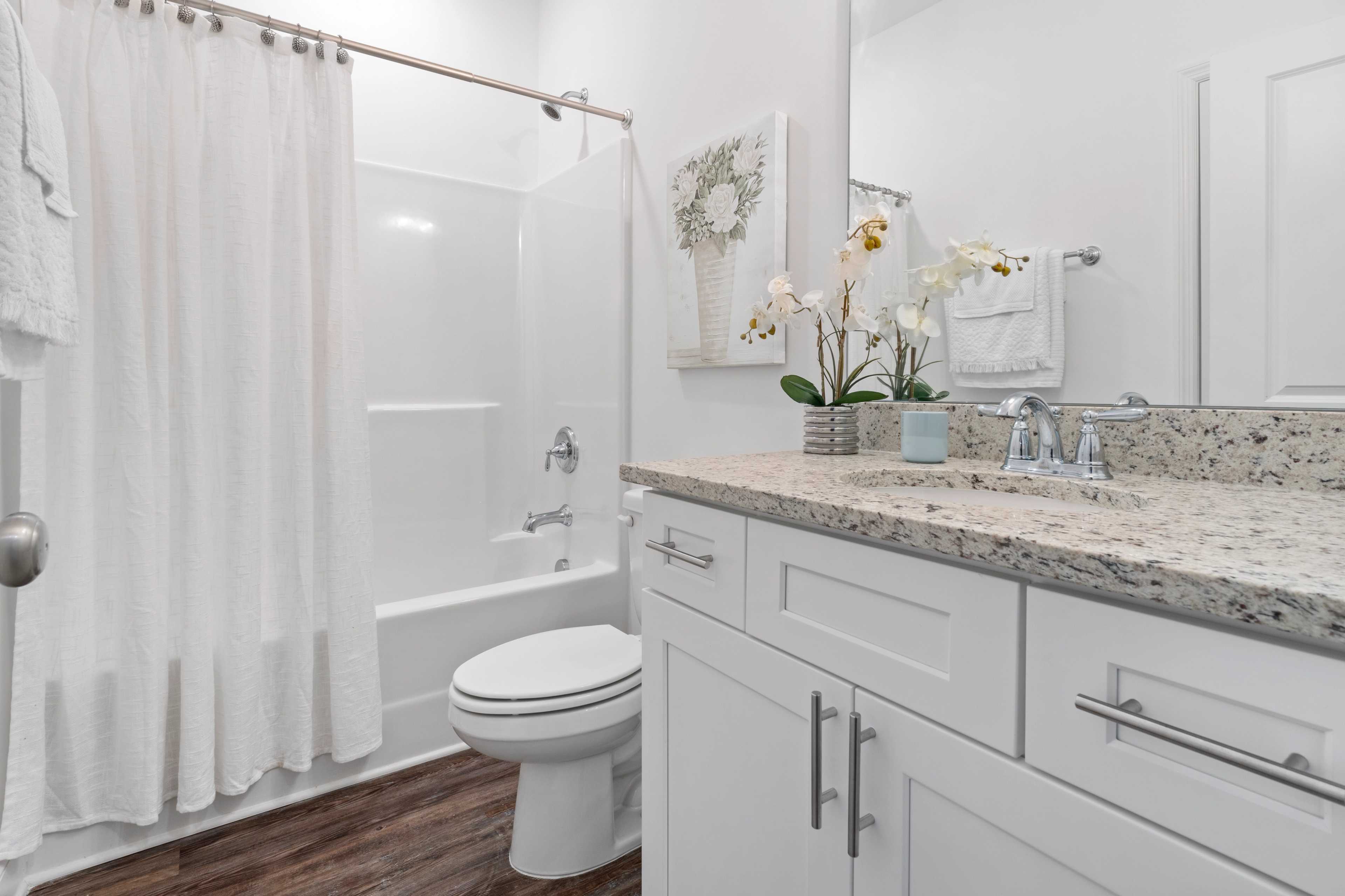 Modern bathroom at The Retreat at Hollon Meadow in Decatur AL with white vanity, granite counters, bathtub, orchids and hardwood floors