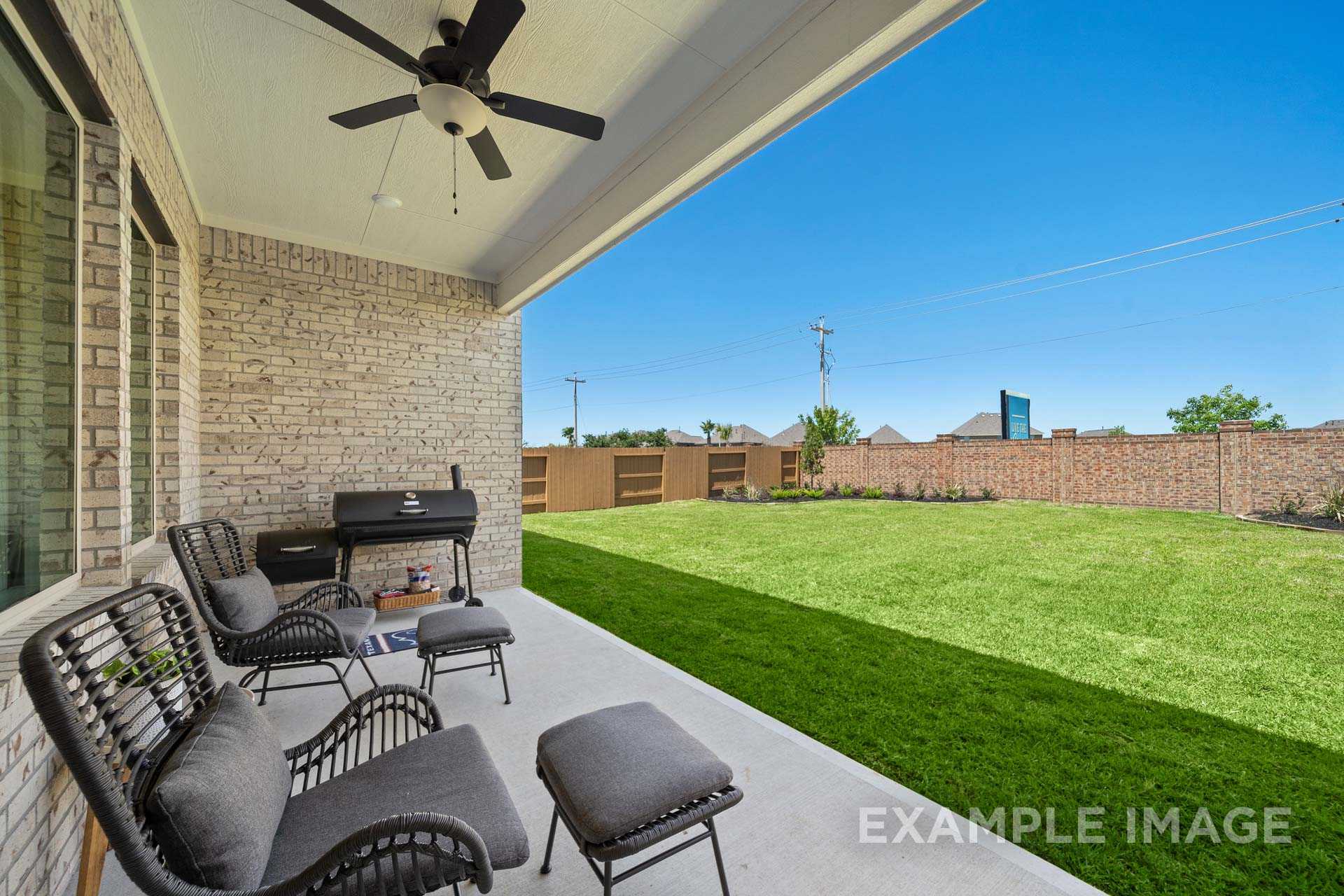Covered patio of The Edward B 3-car garage home featuring ceiling fan, brick exterior, outdoor grill, wicker chairs, and lush green lawn
