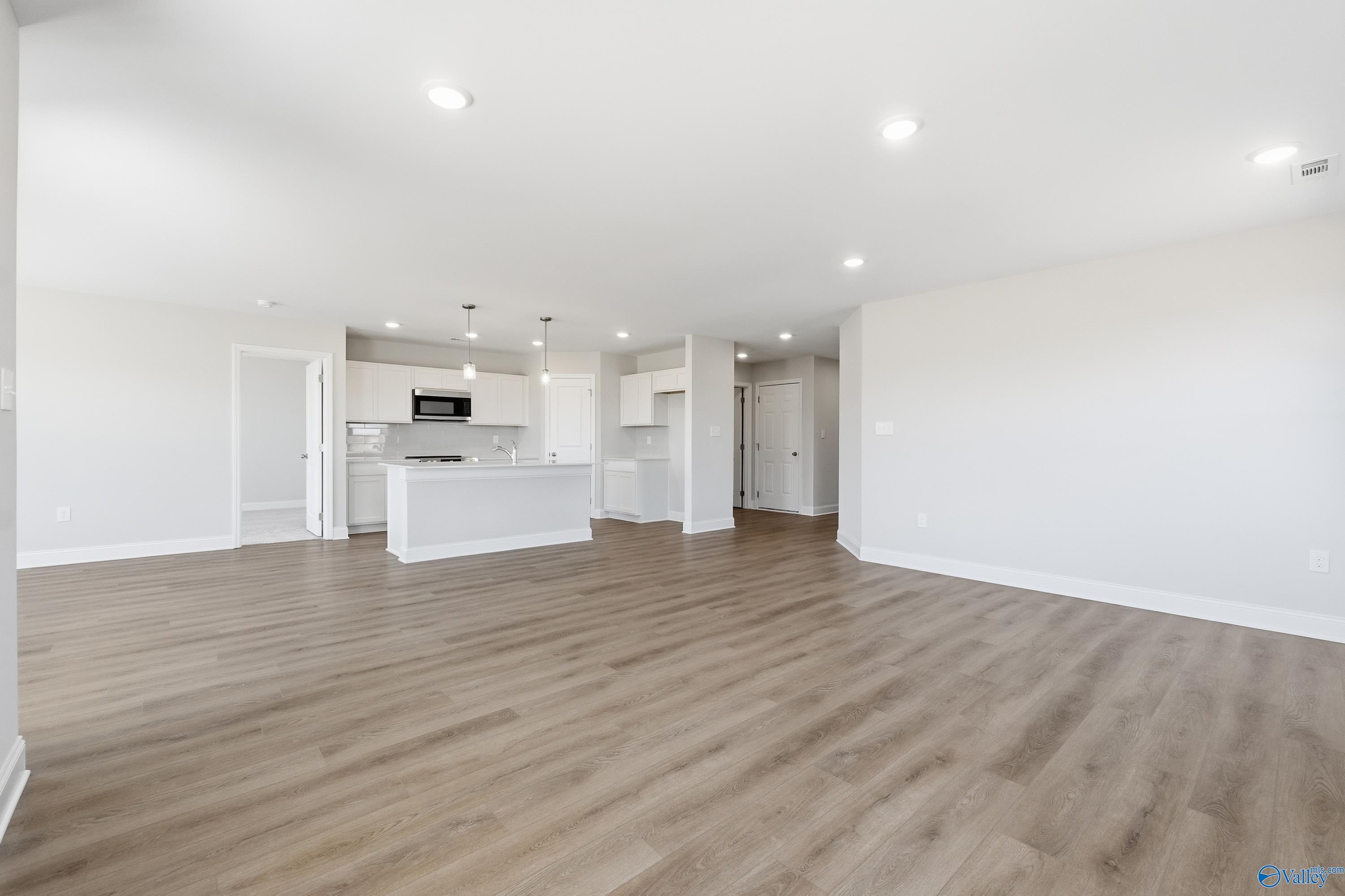 Open-concept living and kitchen area with white cabinets, island, and hardwood floors in Davidson Homes The Franklin, New Market, Alabama