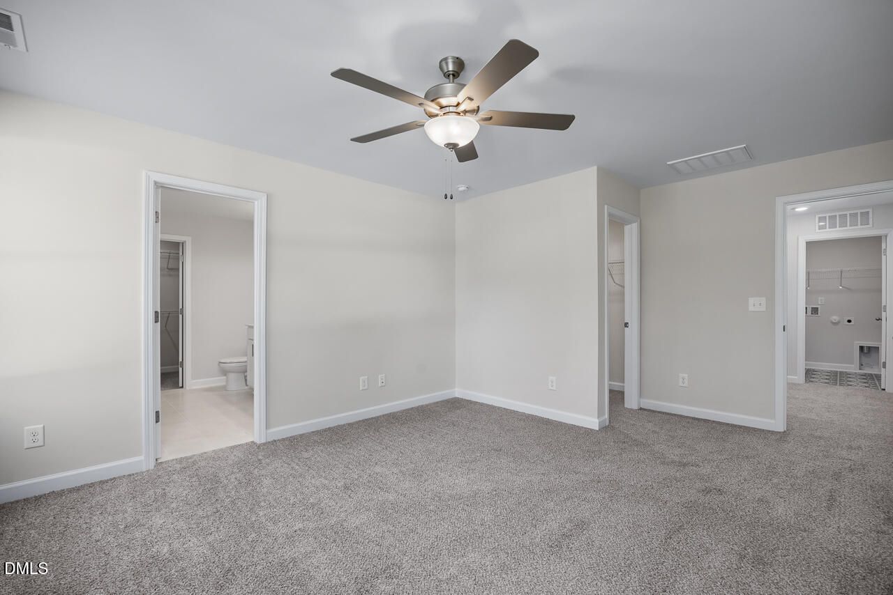 Spacious master bedroom with ceiling fan, neutral walls, carpet floor, and en-suite bath in Davidson Homes The Grace C, Lillington, NC