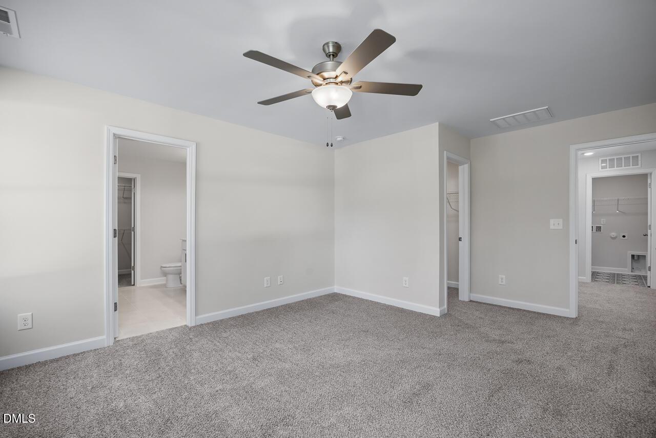 Spacious master bedroom with ceiling fan, neutral walls, carpet floor, and en-suite bath in Davidson Homes The Grace C, Lillington, NC