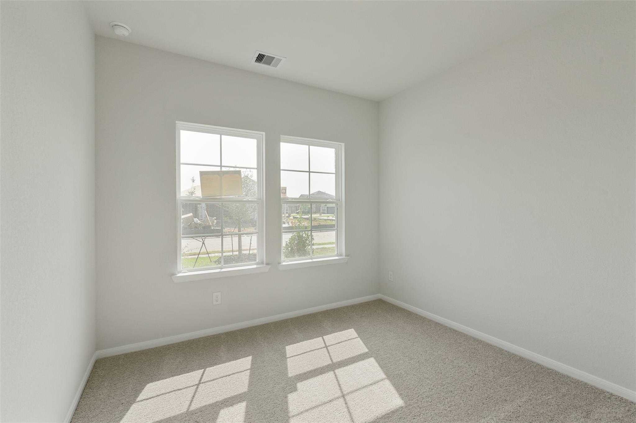 Bright empty secondary bedroom with large windows, beige carpet, and neutral walls in Davidson Homes The Laguna B, Dayton, Texas