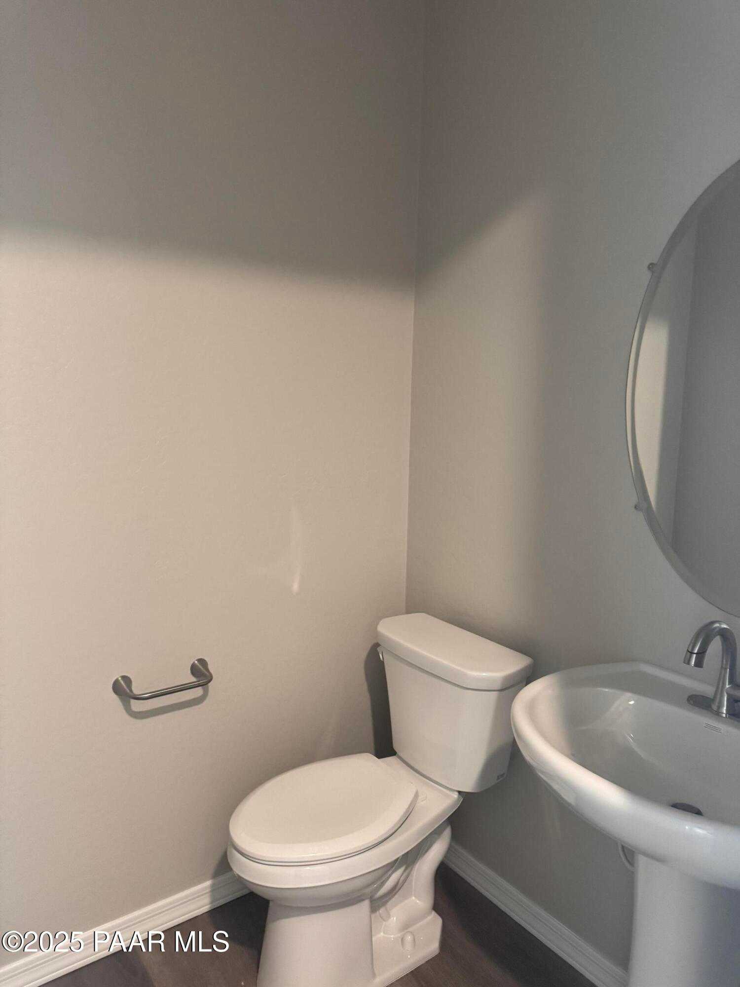 Clean powder room with white toilet, pedestal sink, round mirror, and grab bar in Davidson Homes The Monarch E, Prescott, Arizona