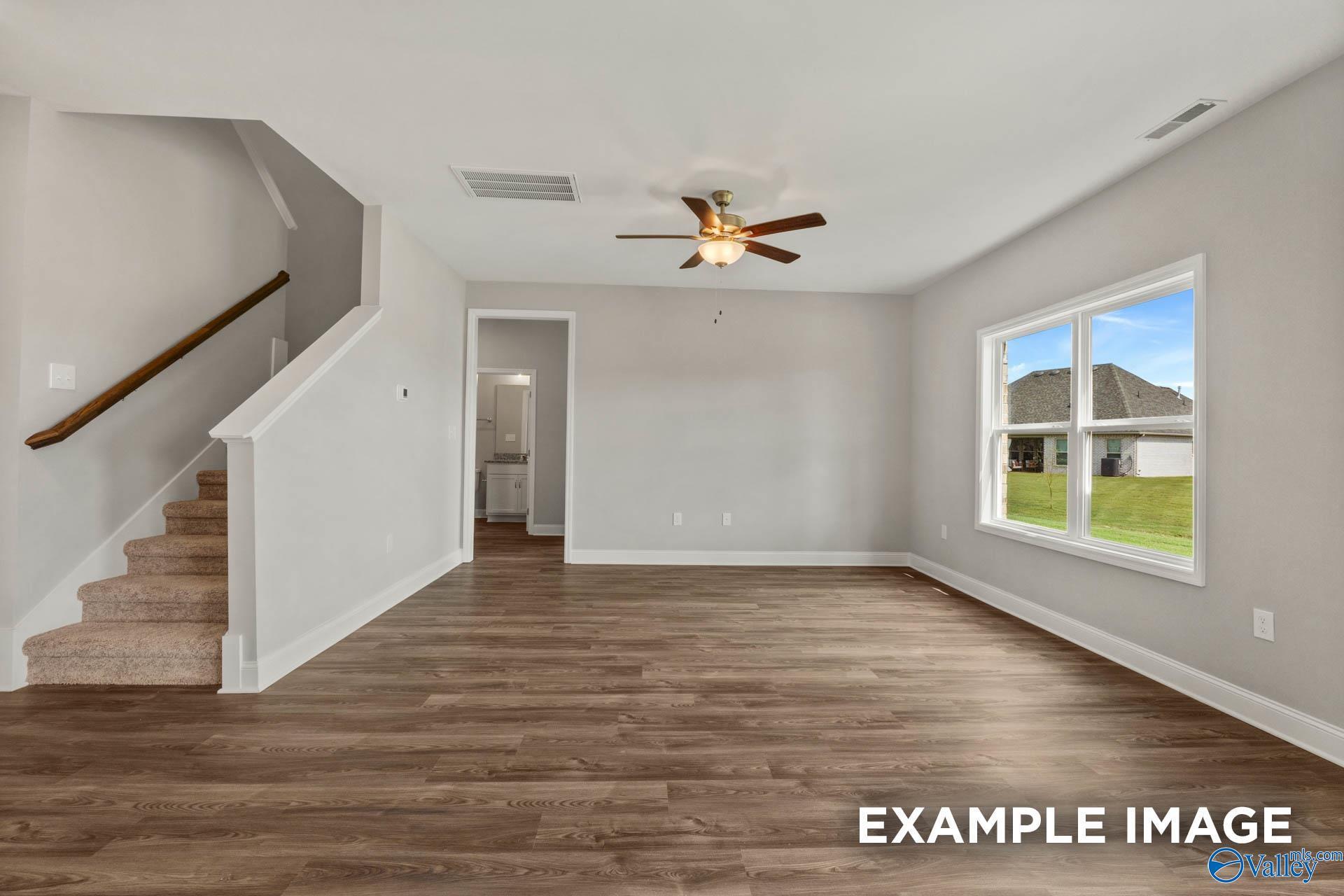 Bright two-story living room with hardwood floors, carpeted staircase, ceiling fan, and window view of green lawn in Davidson Homes Shelby B, New Market, Alabama