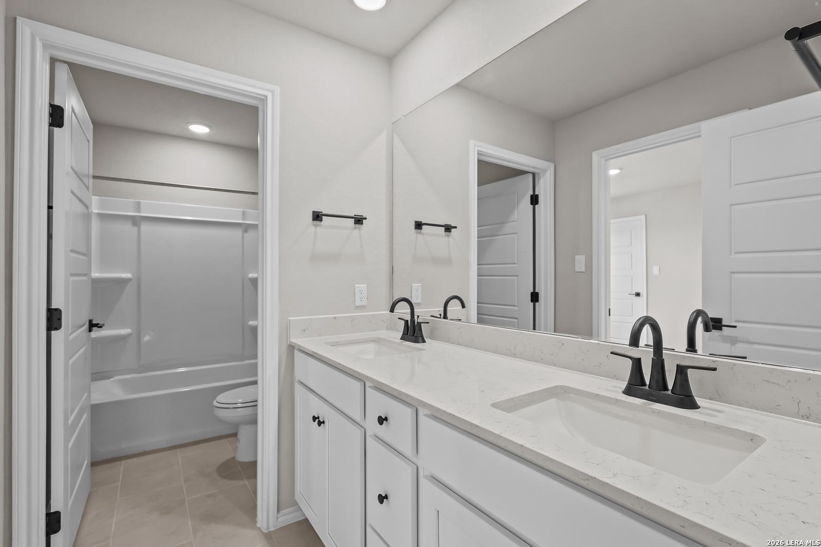 Dual vanity bathroom with white cabinetry, quartz countertops, and black faucets in Davidson Homes Sequoia C, San Antonio