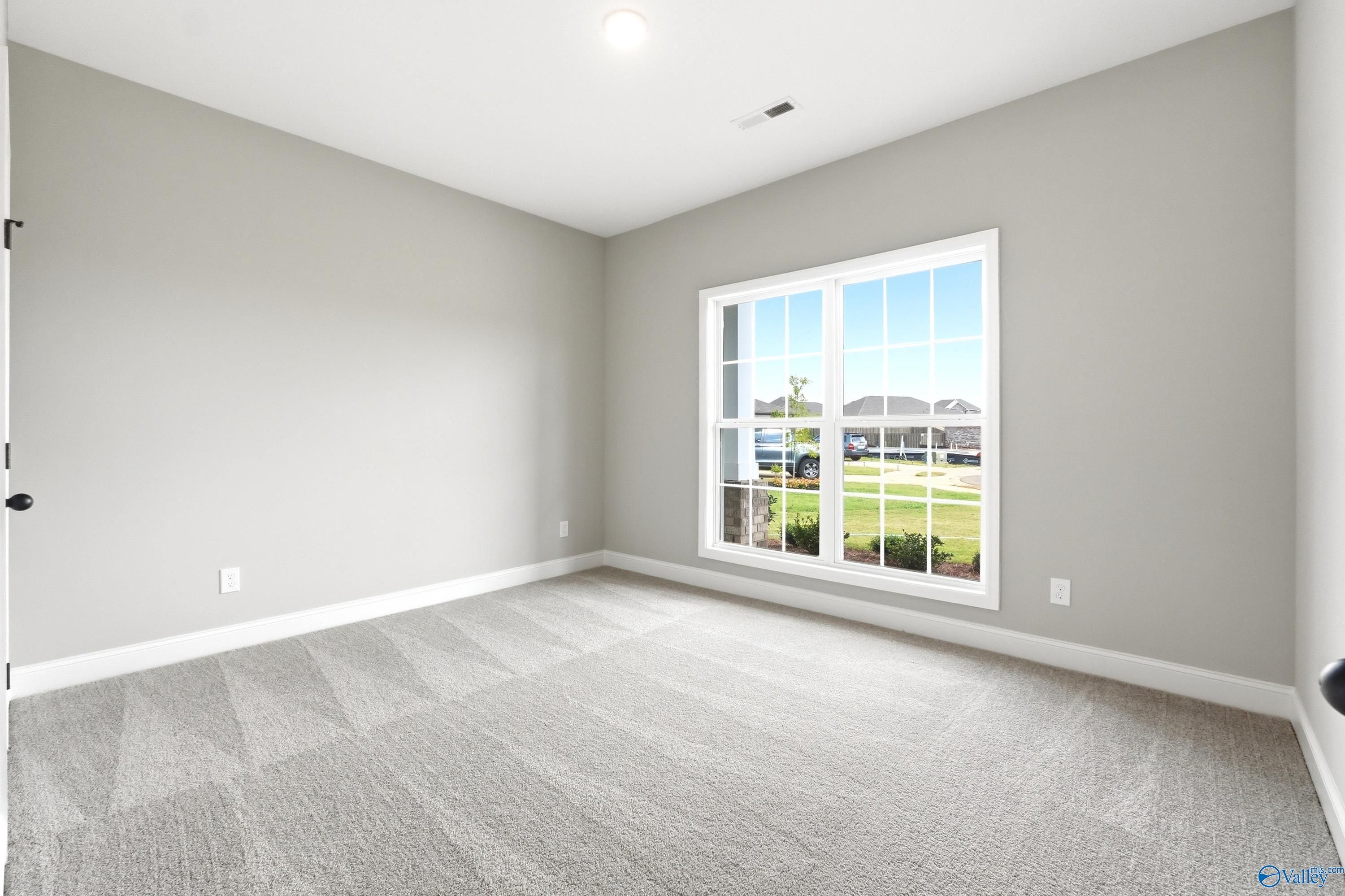 Bright, carpeted bedroom with large window in The Daphne D floor plan by Davidson Homes in Creekside, Harvest, Alabama.