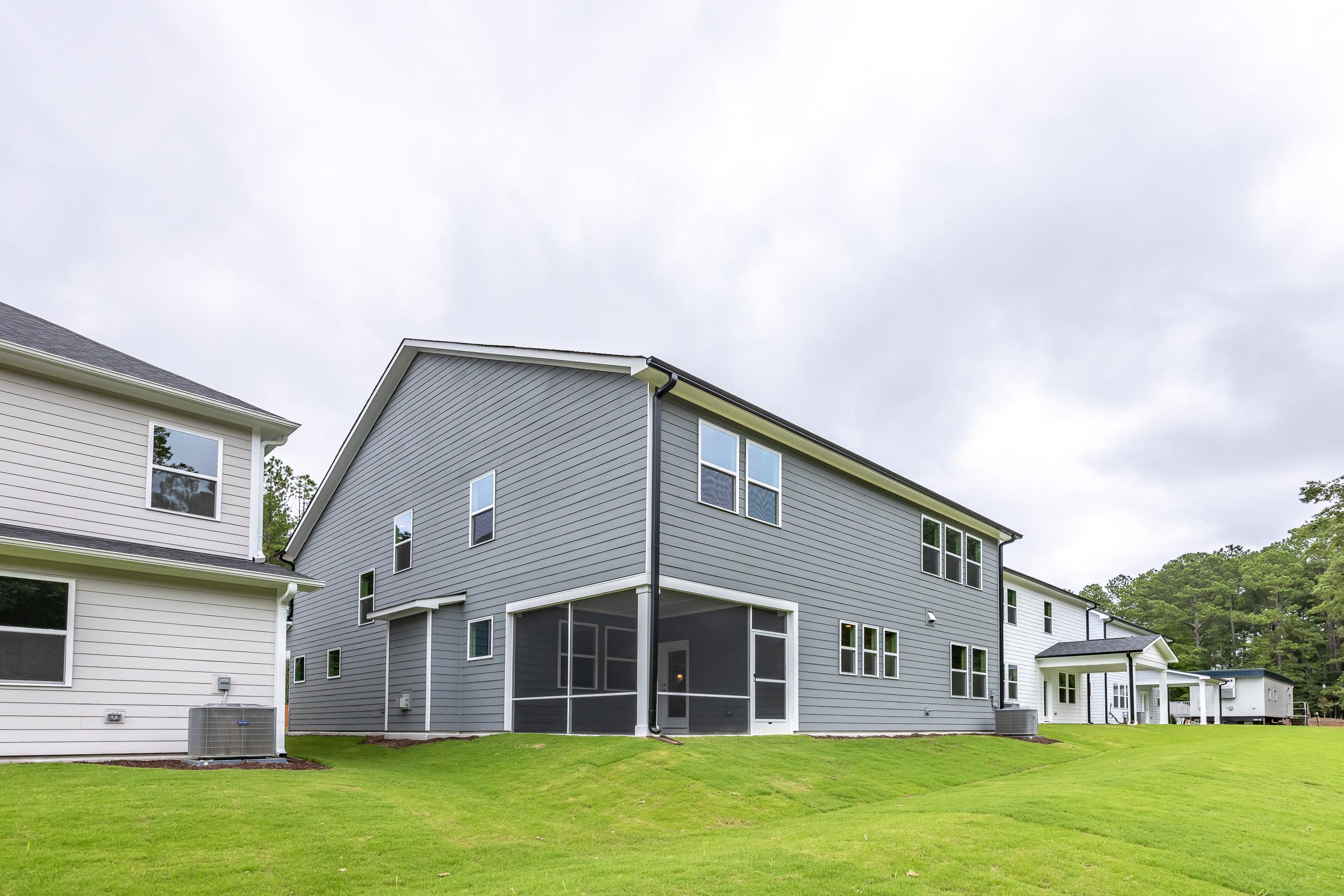 Two-story The Aspen home in Holly Springs NC with gray vinyl siding, brick exterior, screened porch, two-car garage, and lush green lawn