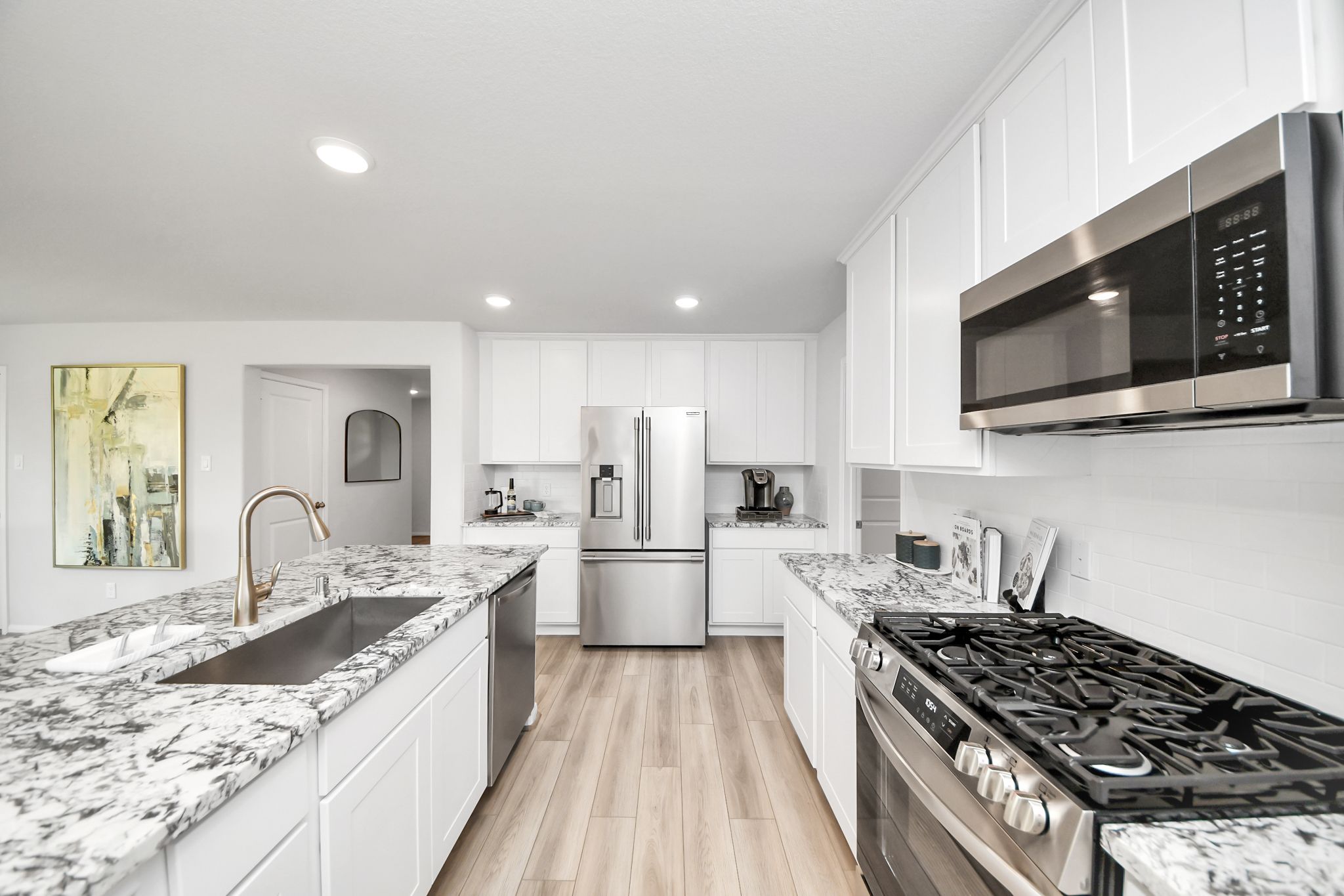 Modern white kitchen in Sunterra, Katy with granite countertops, stainless steel appliances, and wood-look flooring.