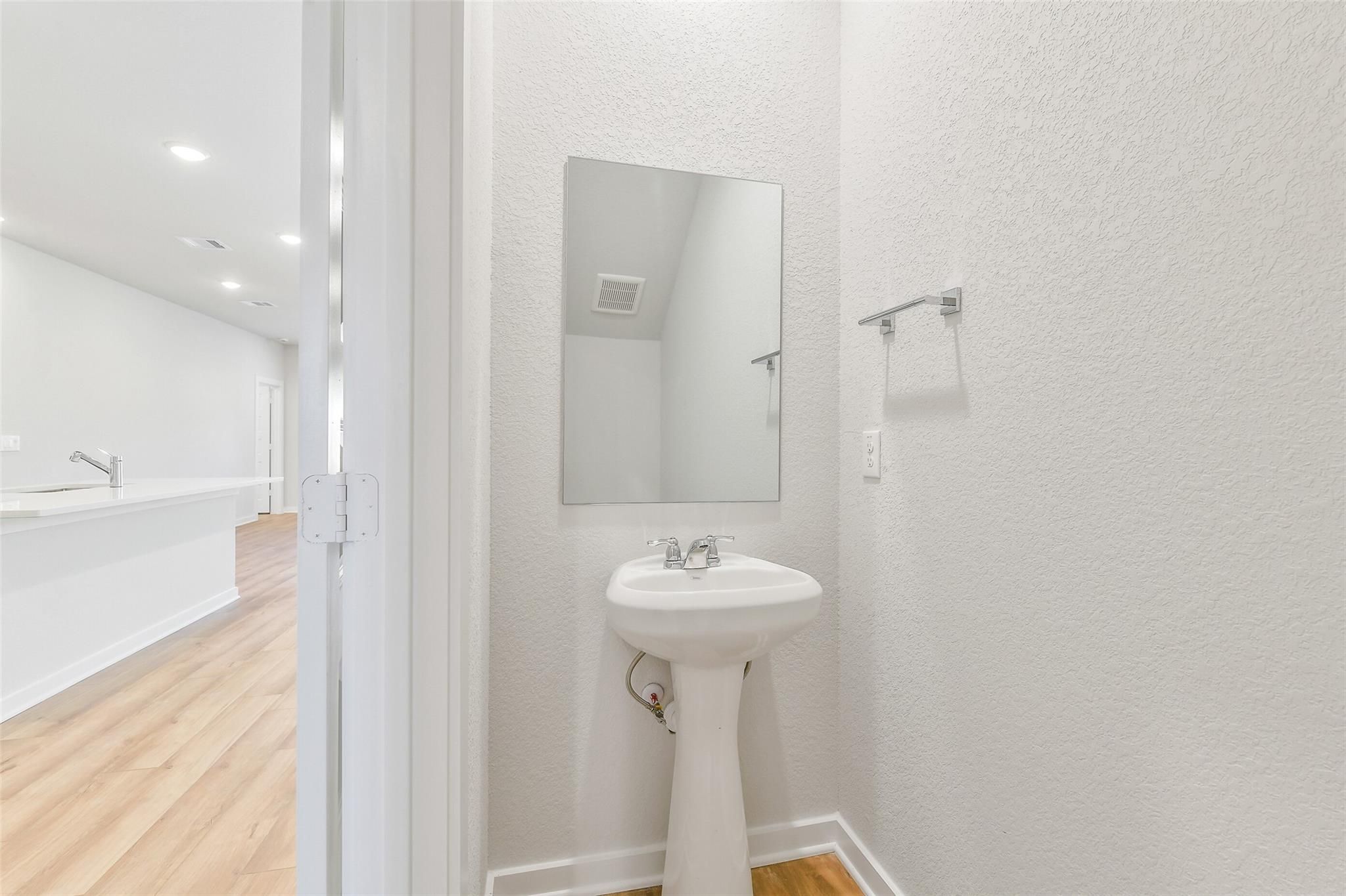 Bright powder room with white pedestal sink and mirror in Davidson Homes The Blanco E, Magnolia, Texas