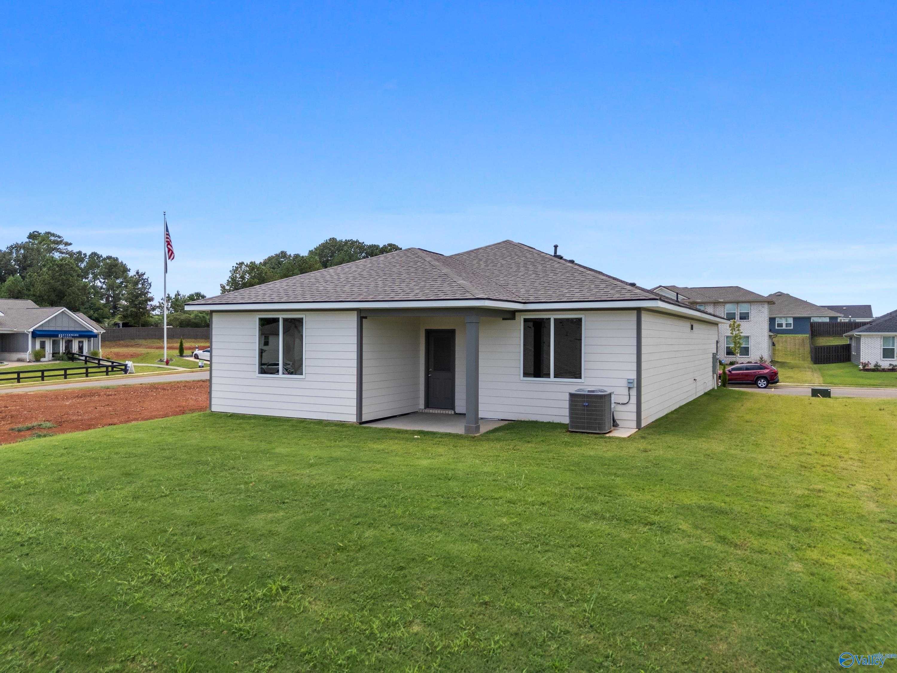 Modern white single-story home with 2-car garage, American flag, and green lawn in Evergreen Mill, Madison, Alabama - Evermore Homes The Malibu