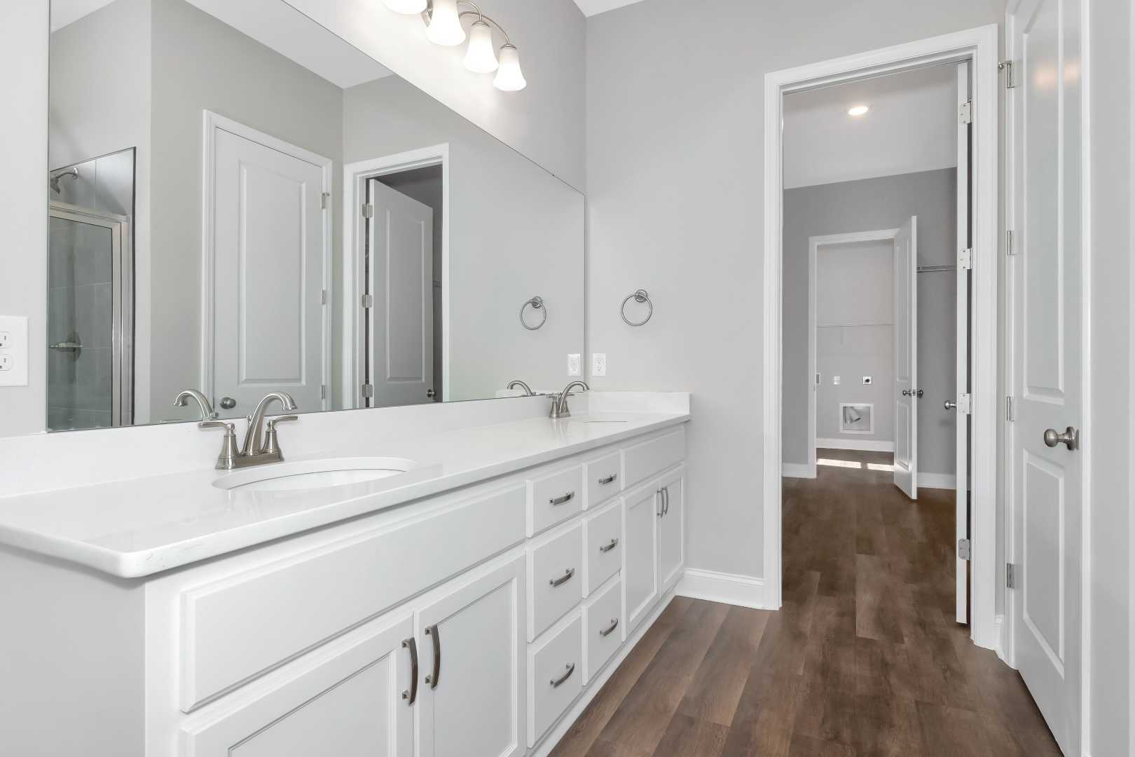 Spacious master bathroom in The Arcadia M with double white vanity, large mirror, walk-in shower, gray walls