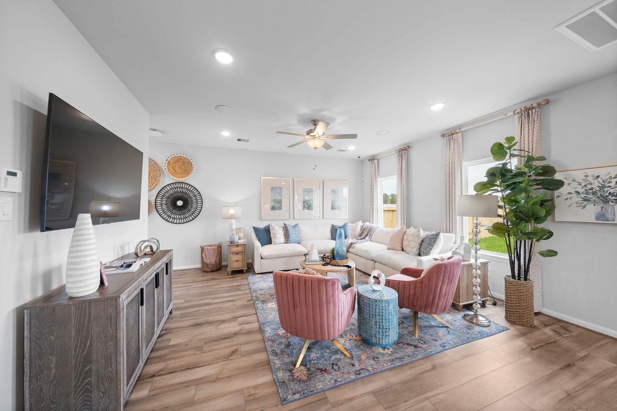 Bright living room with sectional sofa, blush accent chairs, wood-look floors in Davidson Homes Trinity F plan, Splendora, TX