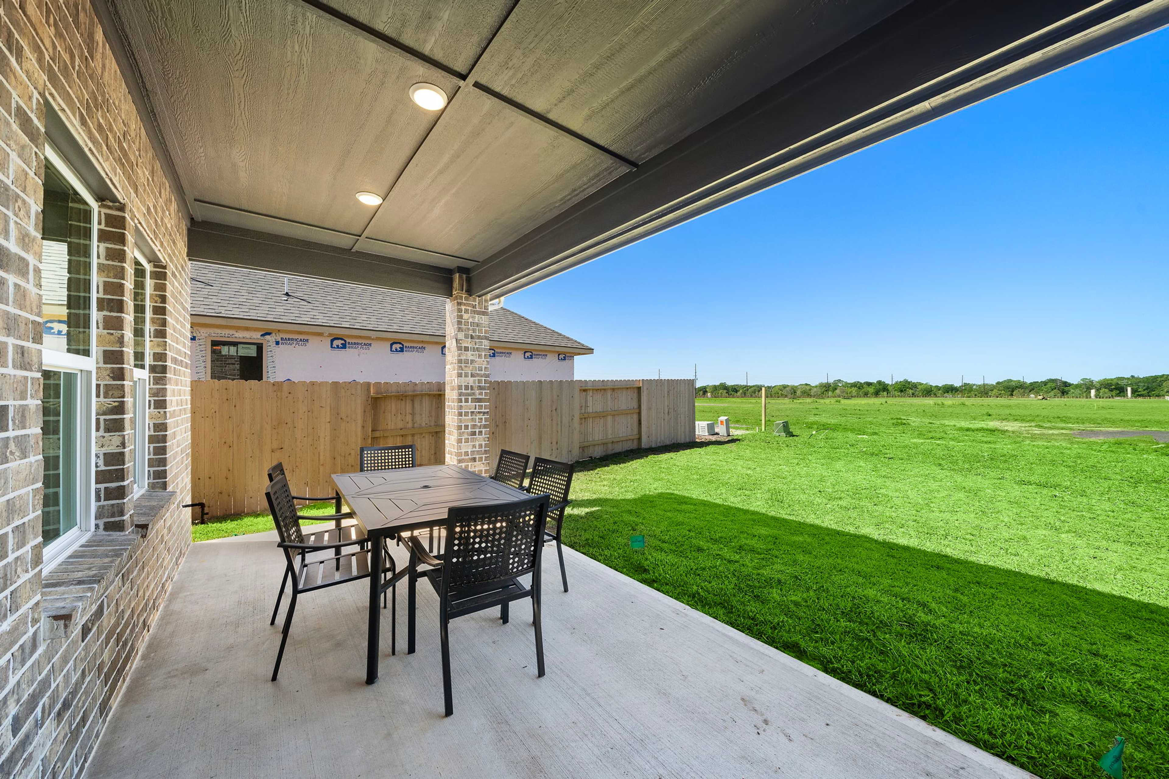 Spacious covered patio with brick accents and outdoor dining set at Emberly in Beasley, Texas overlooking lush green lawn