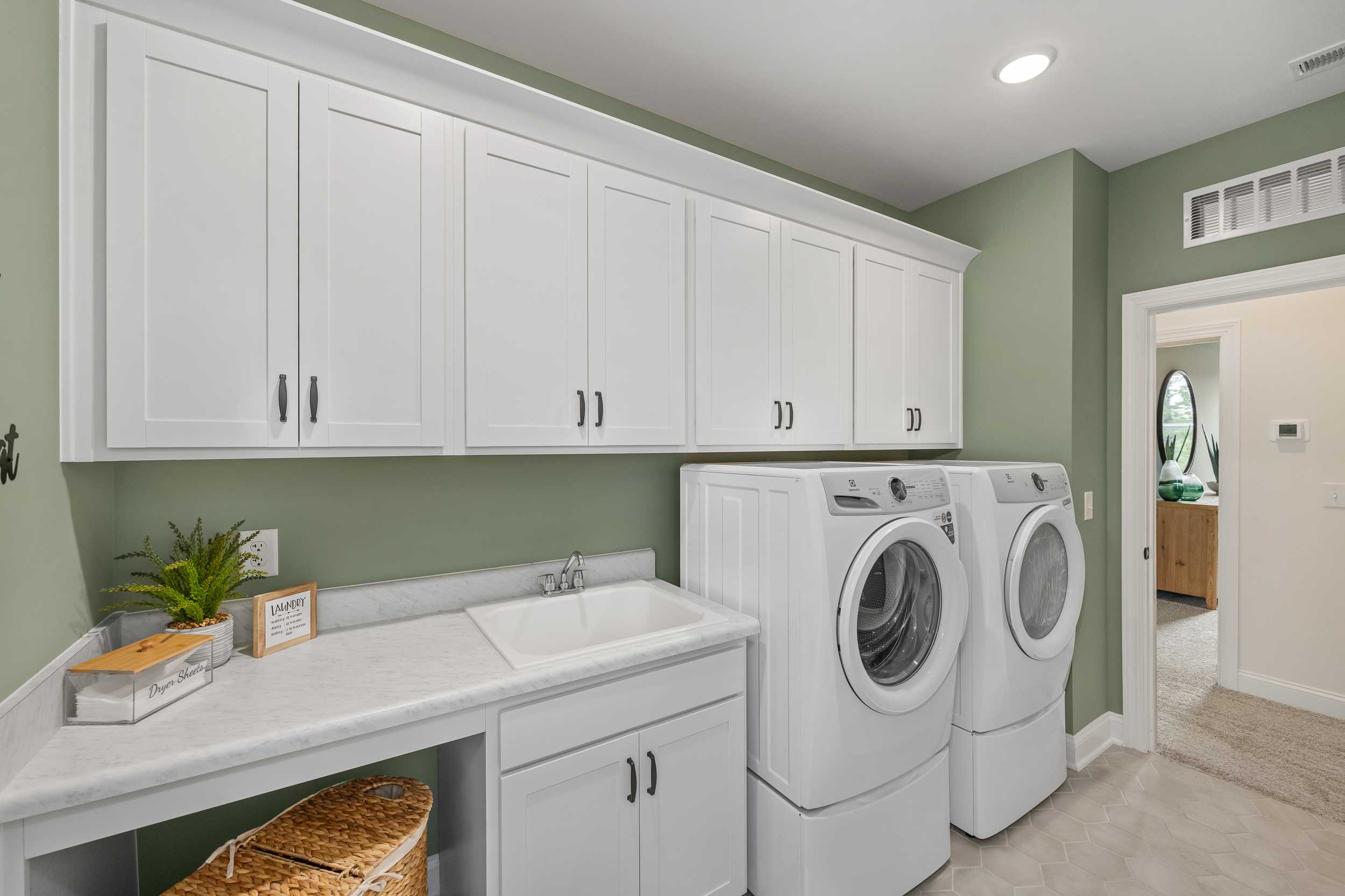 Spacious laundry room in Laneridge Estates, Raleigh NC with white shaker cabinets, green walls, washer-dryer duo, utility sink