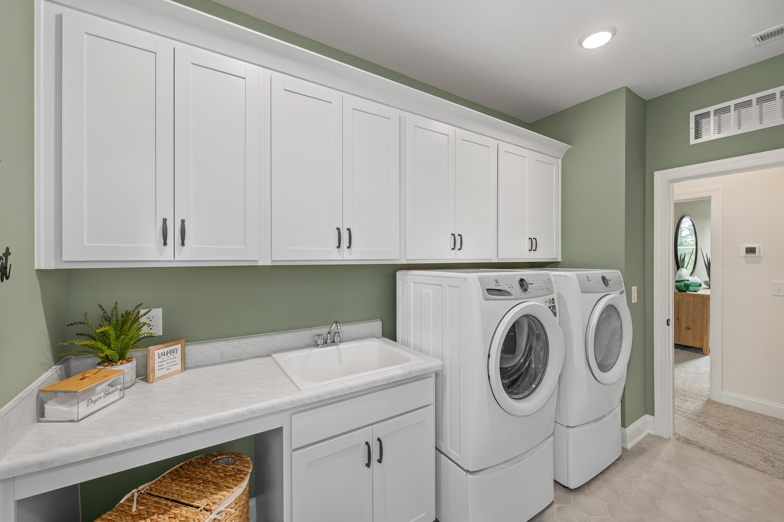 Spacious laundry room in Laneridge Estates, Raleigh NC with white shaker cabinets, green walls, washer-dryer duo, utility sink