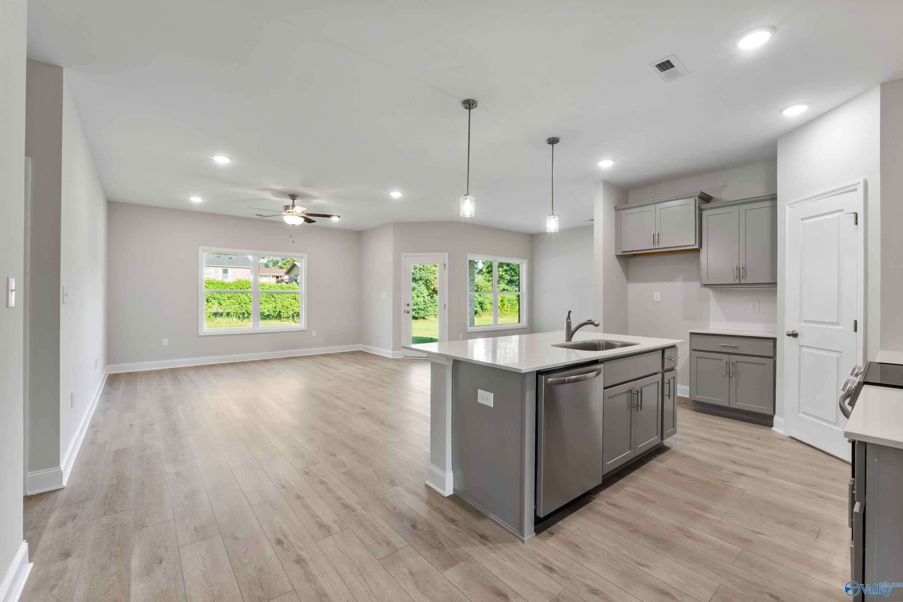 Open-concept kitchen-living area with gray shaker cabinets, large island sink, hardwood floors, and backyard views in The Daphne C, Huntsville, AL