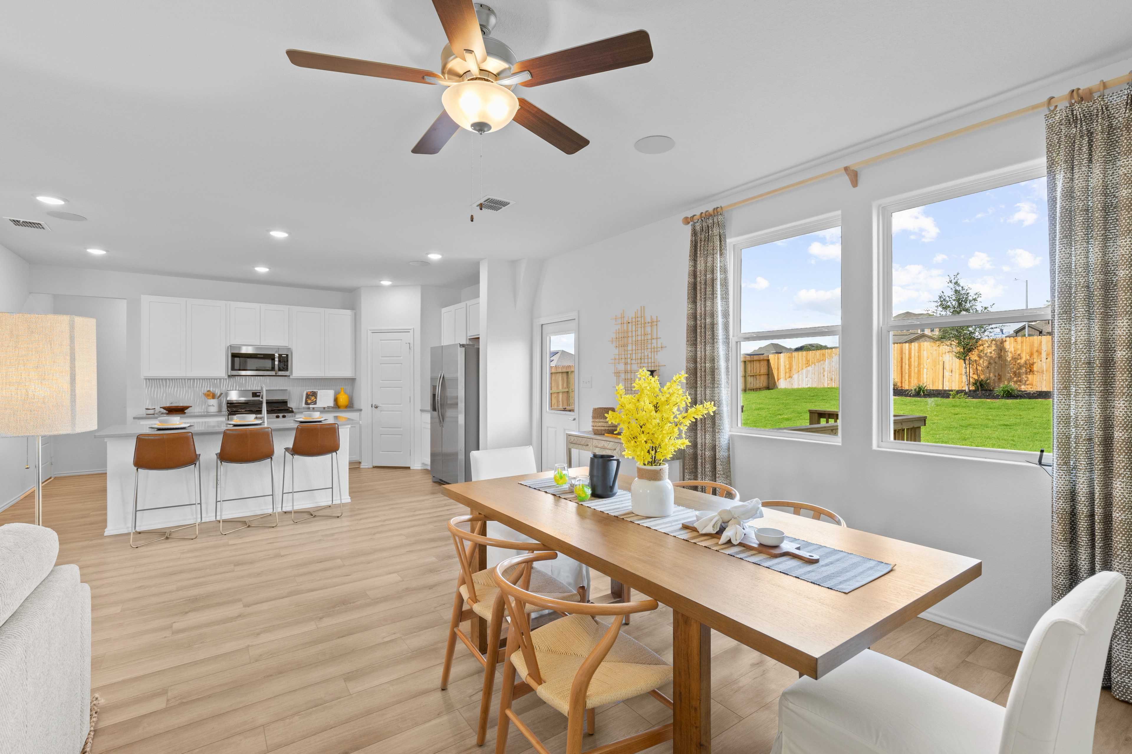 Open-concept kitchen dining area at Horizon Pointe in Converse Texas by Davidson Homes with white cabinets hardwood floors and backyard view