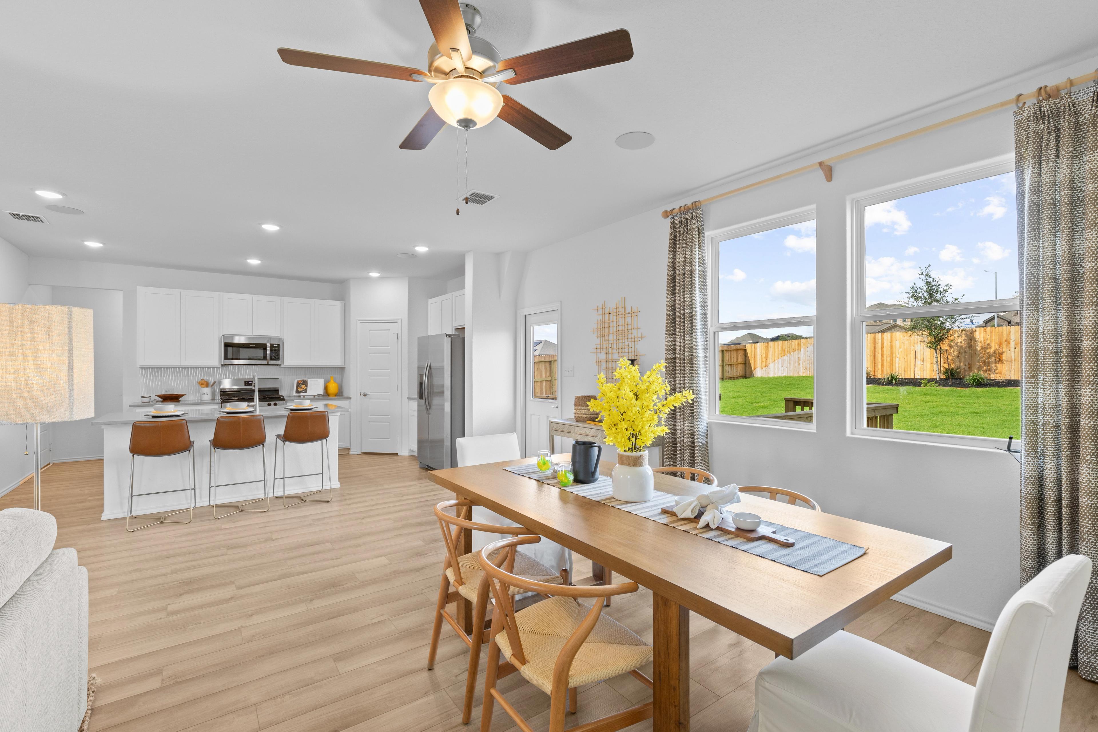 Open-concept kitchen dining area at Horizon Pointe in Converse Texas by Davidson Homes with white cabinets hardwood floors and backyard view